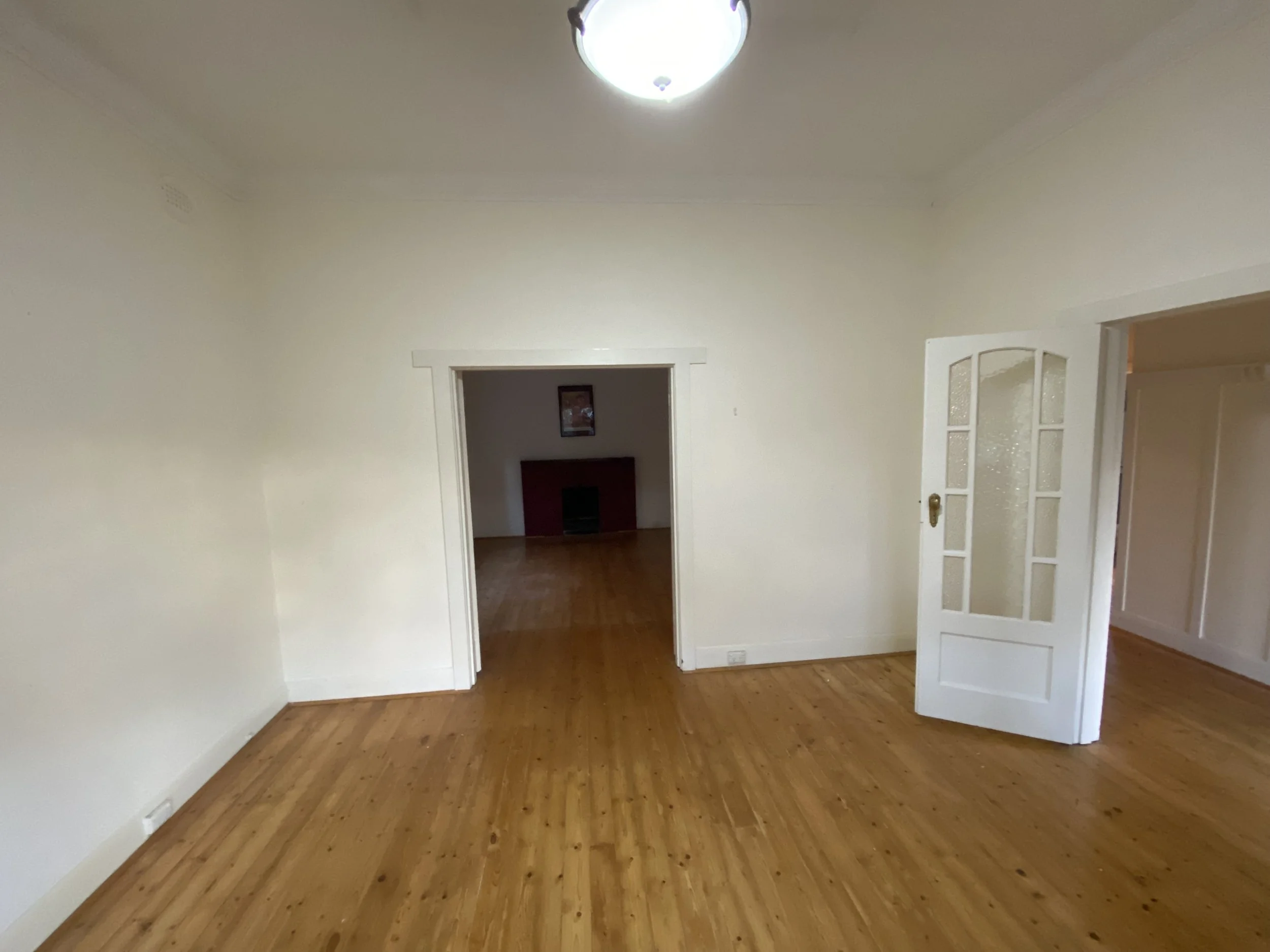 Empty room with wooden floor, cream-colored walls, doorway, and a partial view into another room.