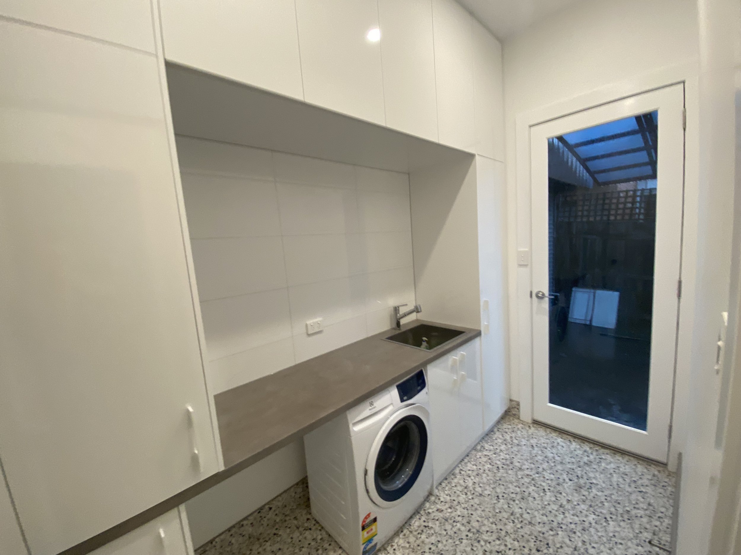 A laundry room with white cabinets, a countertop, a washing machine, and a door leading outside.
