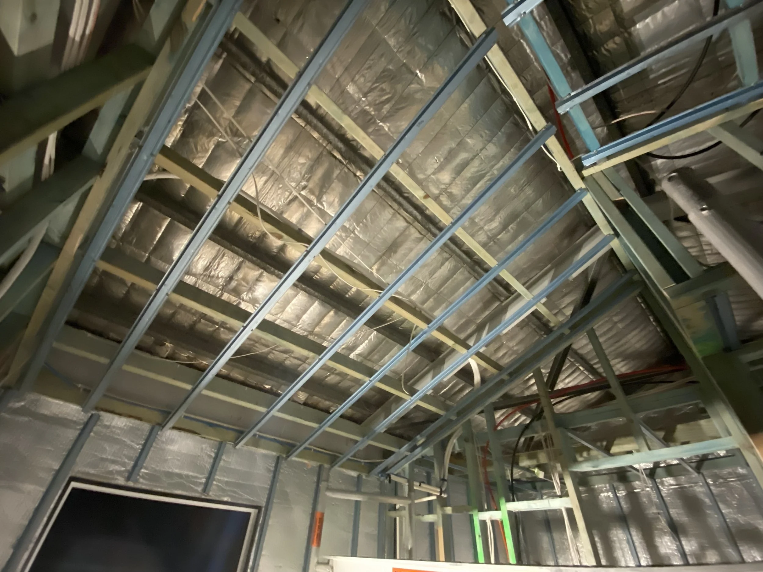 View of an unfinished interior with exposed metal framework, insulation, and wiring, indicating a building under construction or renovation.
