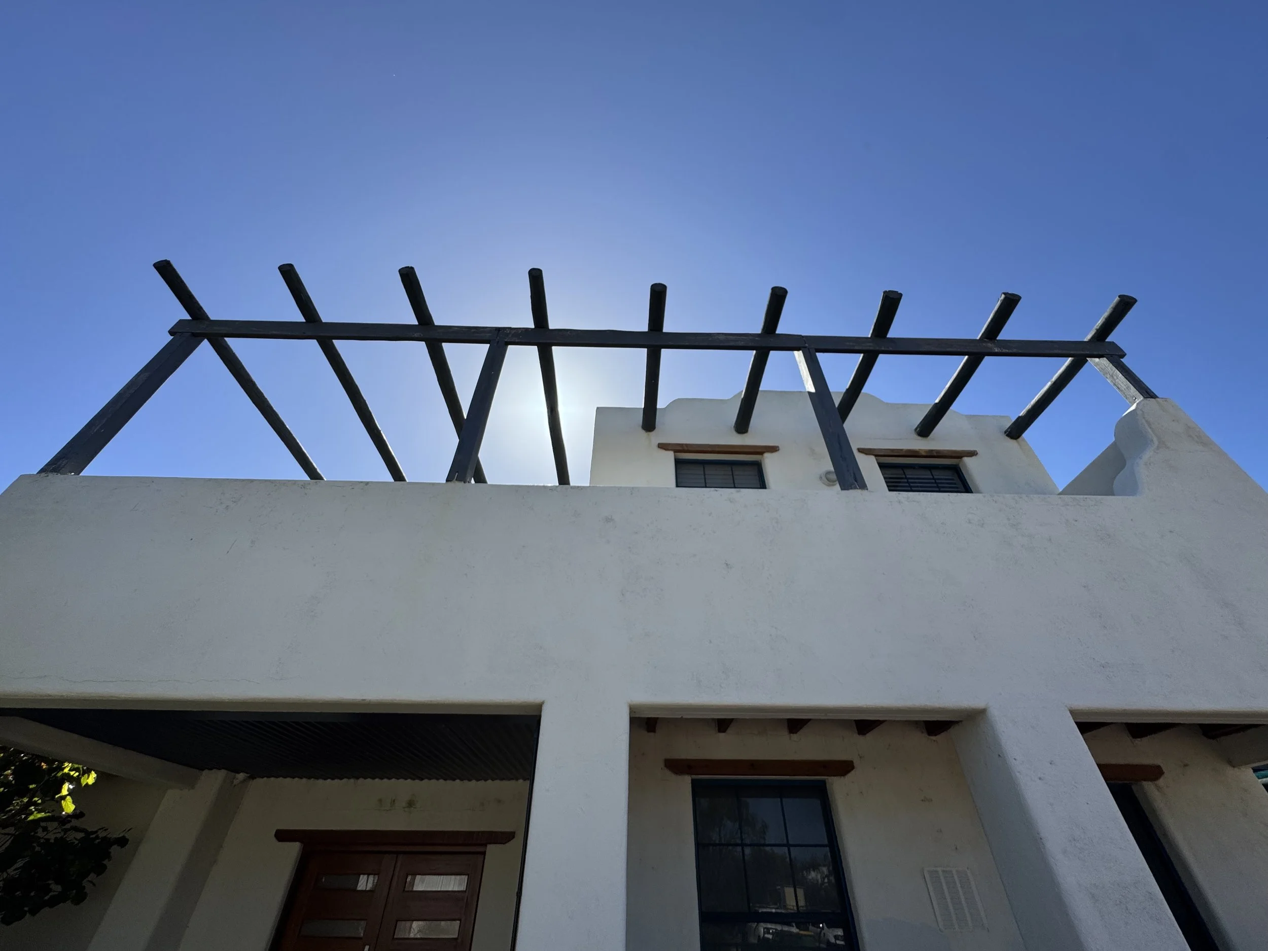 A white building with a curved roof, wooden window frames, and black decorative beams on the upper part of the exterior wall, against a clear blue sky.