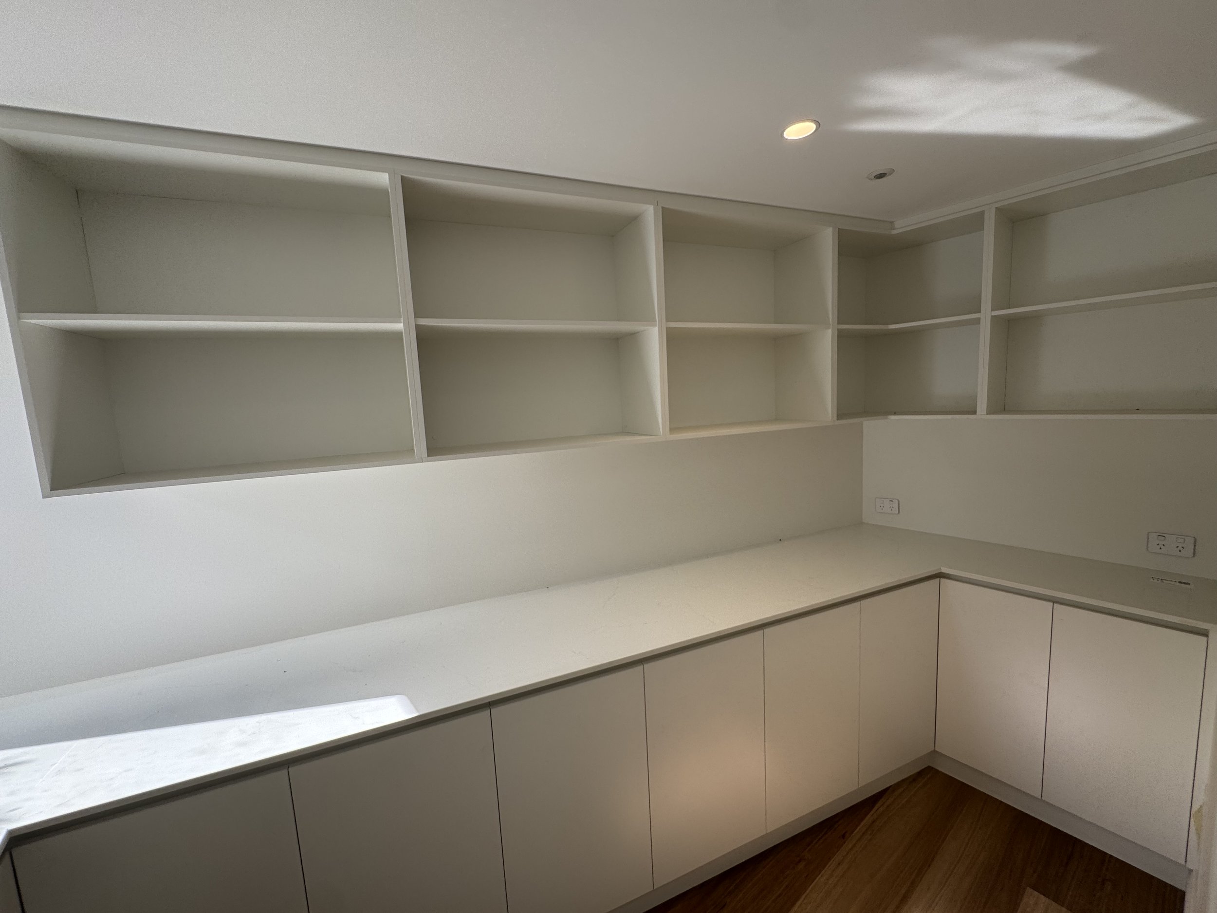 Empty white built-in shelves and cabinetry in a room with wood flooring and electrical outlets on the wall.