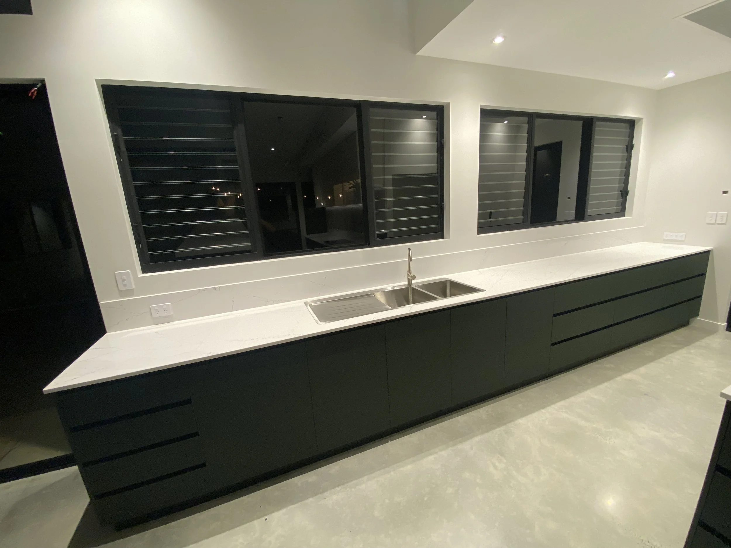 Modern kitchen with white countertop, black cabinets, large black-framed windows, and a stainless steel sink.