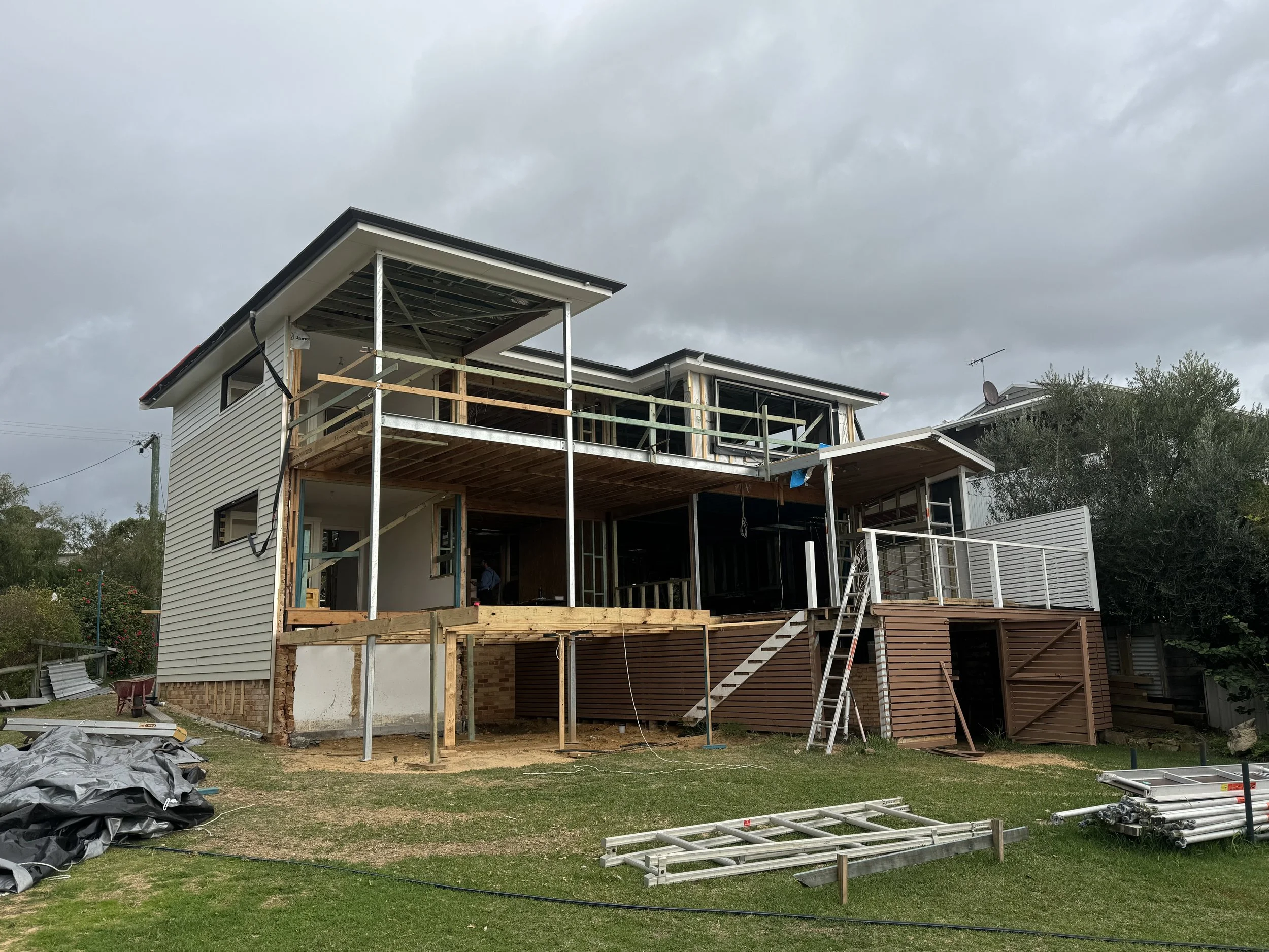 Two-story house under construction with scaffolding and building materials on a cloudy day.