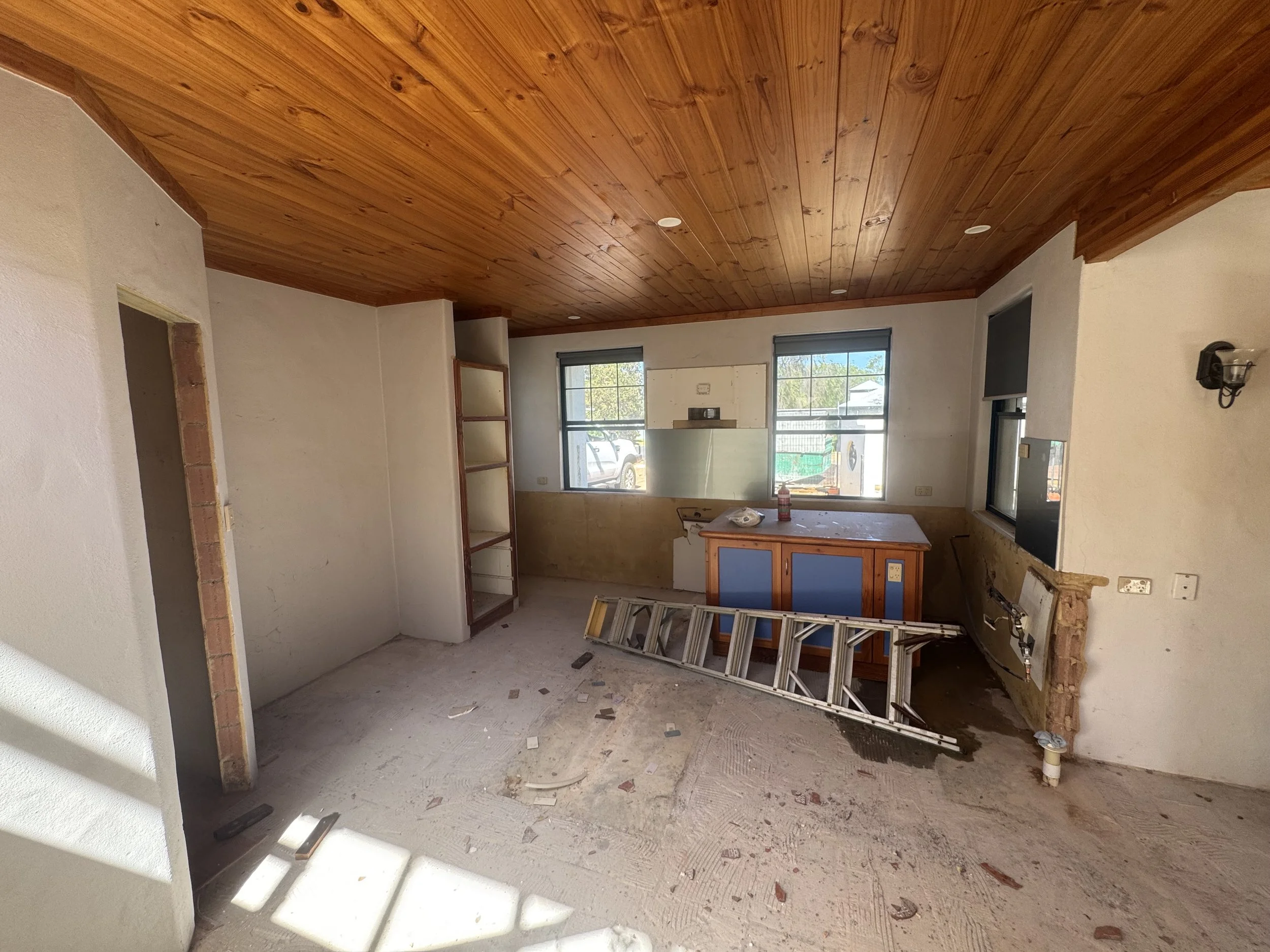 Interior of a house under renovation with a wooden ceiling, a kitchen area, and construction debris on the floor.
