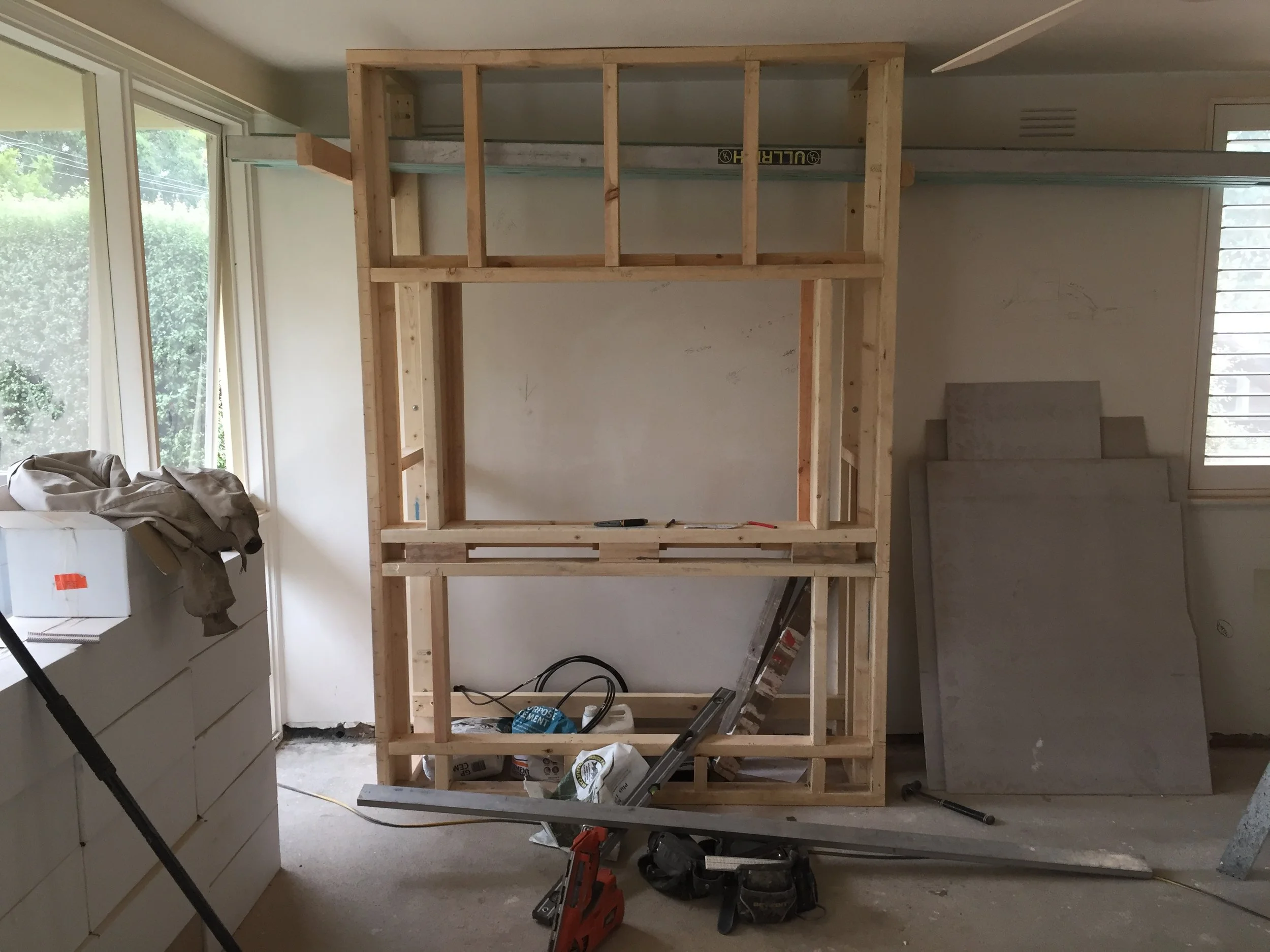 Interior of a room under construction with a wooden frame, drywall, tools, and construction materials.