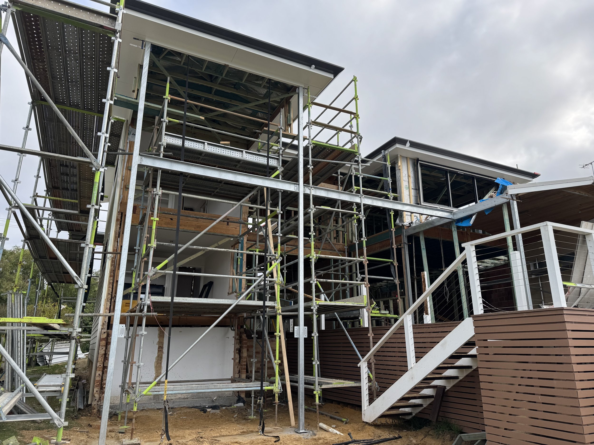 Construction site showing a modern house with scaffolding around the exterior, unfinished walls, and large windows.