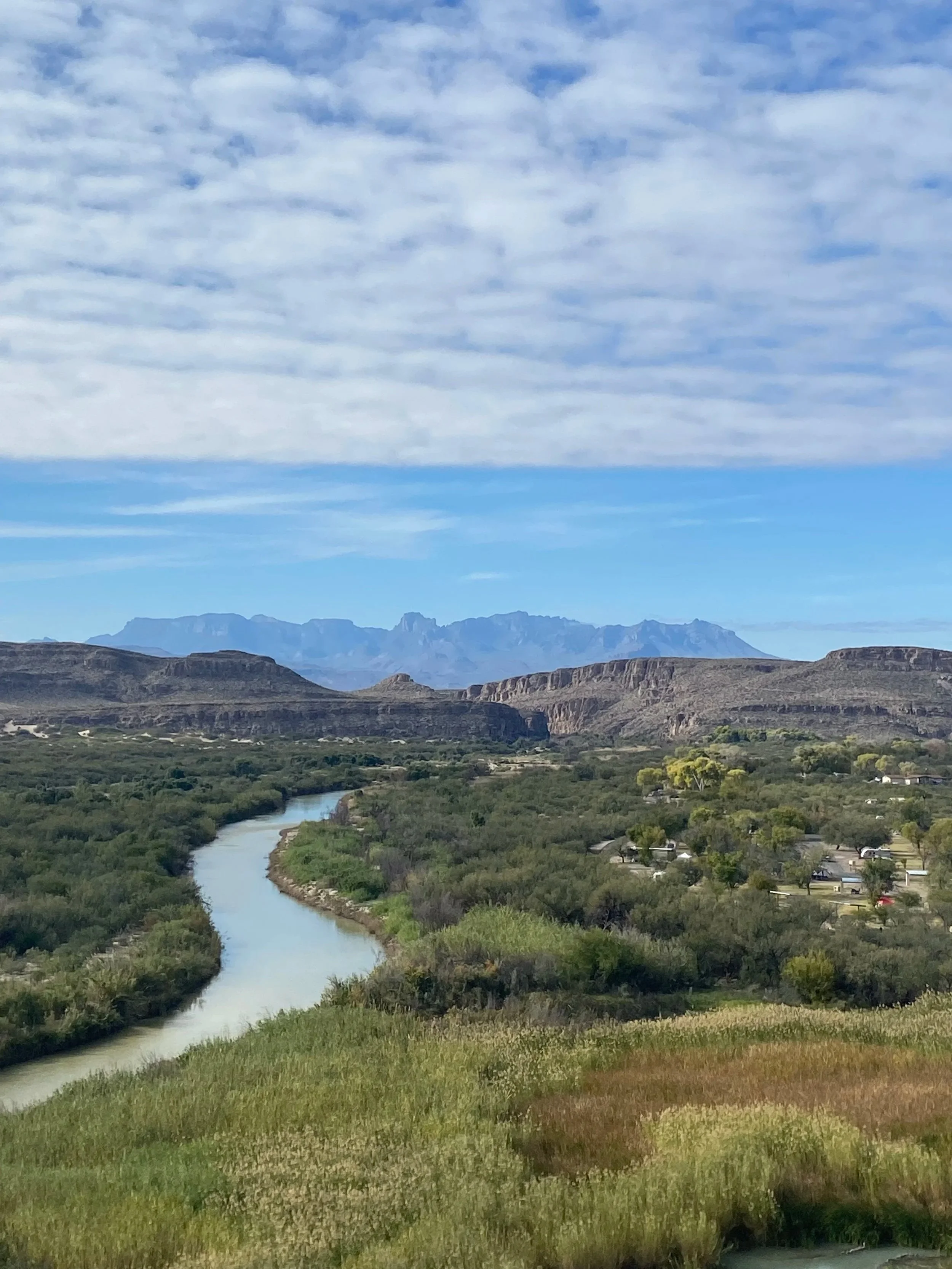 Scenic landscape with a winding river, green fields, distant mountains, and a cloudy sky.