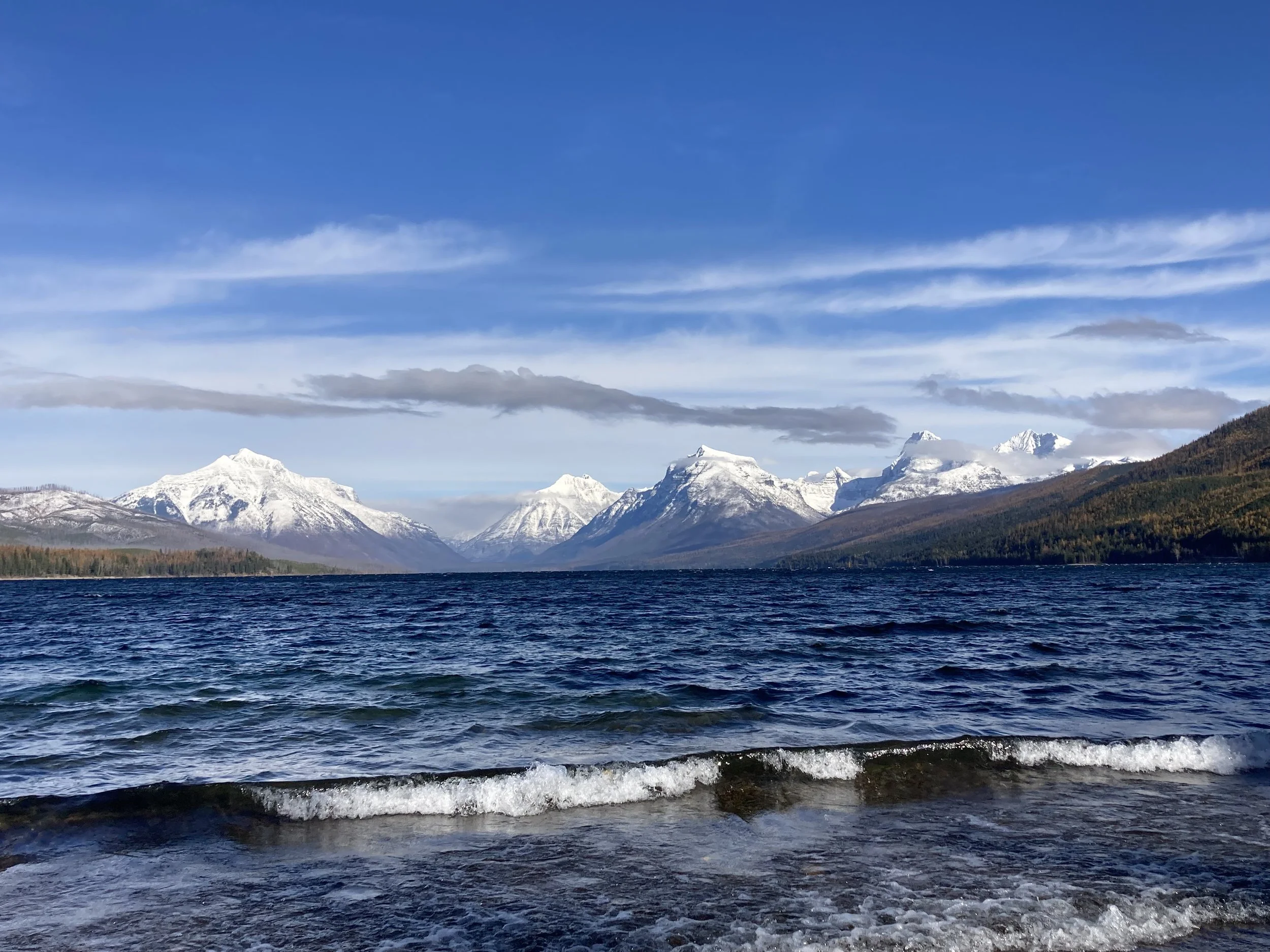 Snow-capped mountains in the distance, with a large body of dark blue water in the foreground, under a partly cloudy sky.