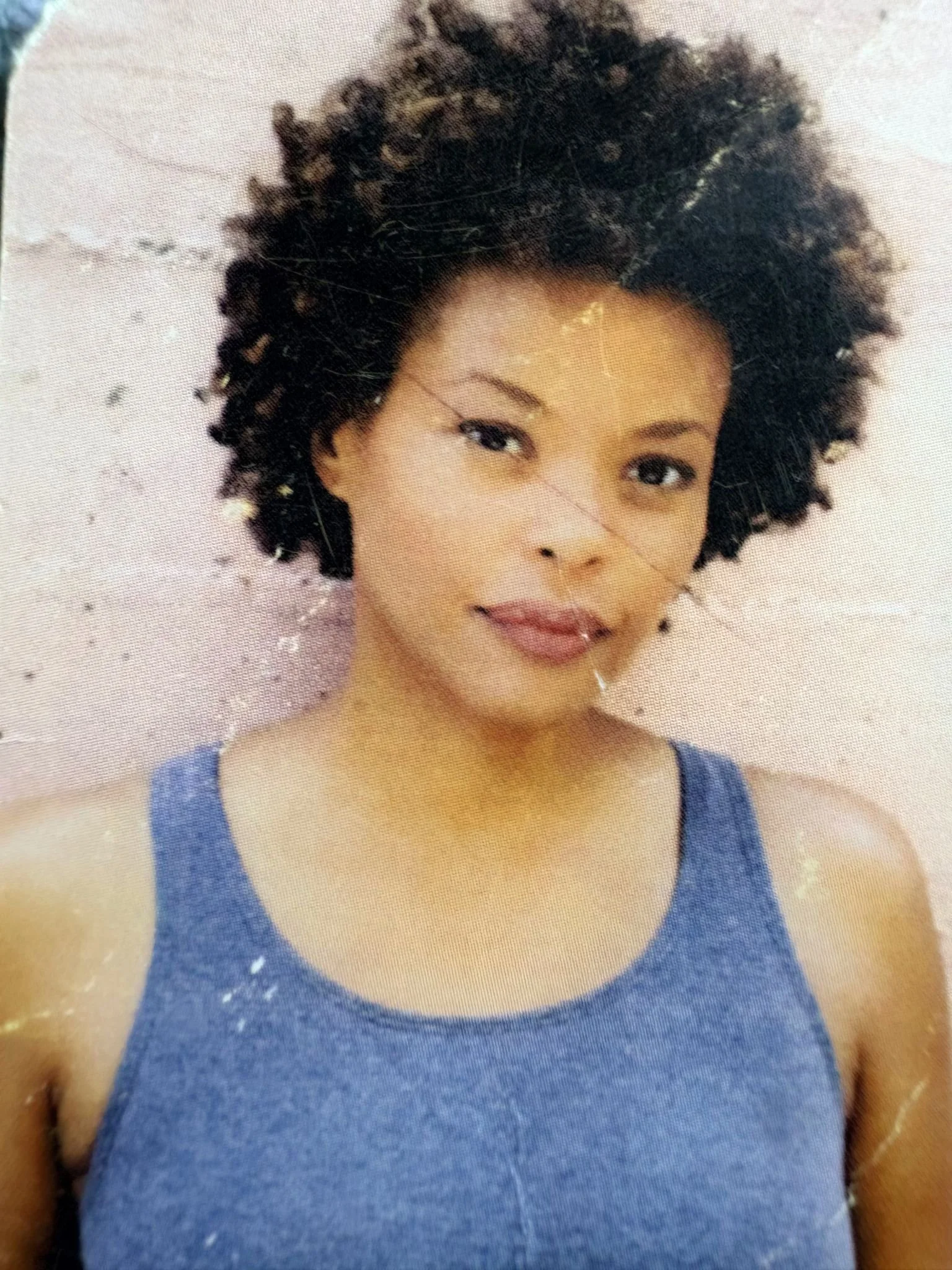 Erickka Jones with short, curly black hair and light skin, wearing a blue sleeveless top, smiling softly against a light background for a commercial shot. 