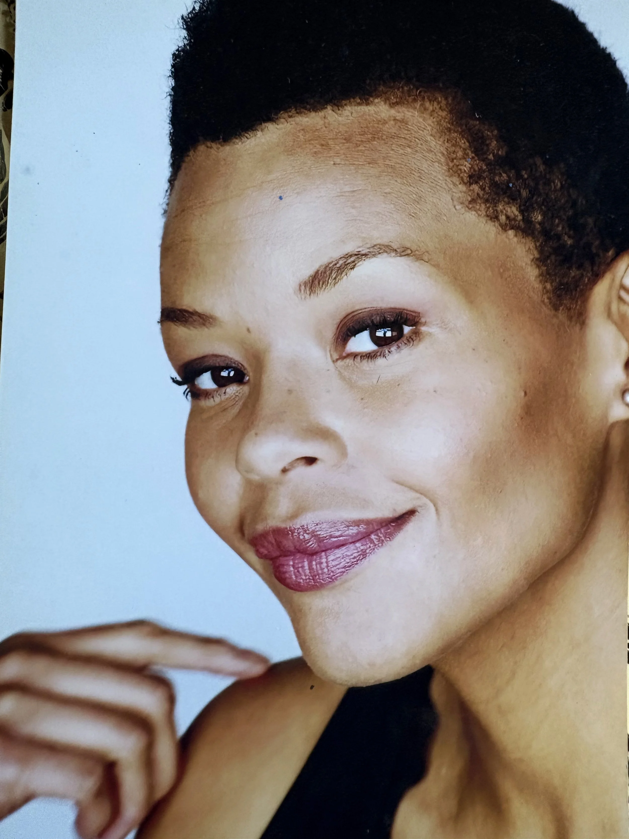 Close-up of Erickka Jones with short dark hair, wearing makeup with pink lipstick, and holding her hand near her face.