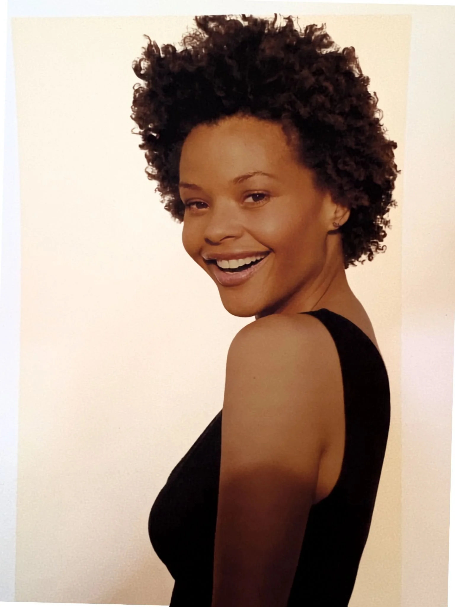 Erickka Jones with short curly hair smiling, wearing a black sleeveless top, with a plain light-colored background.