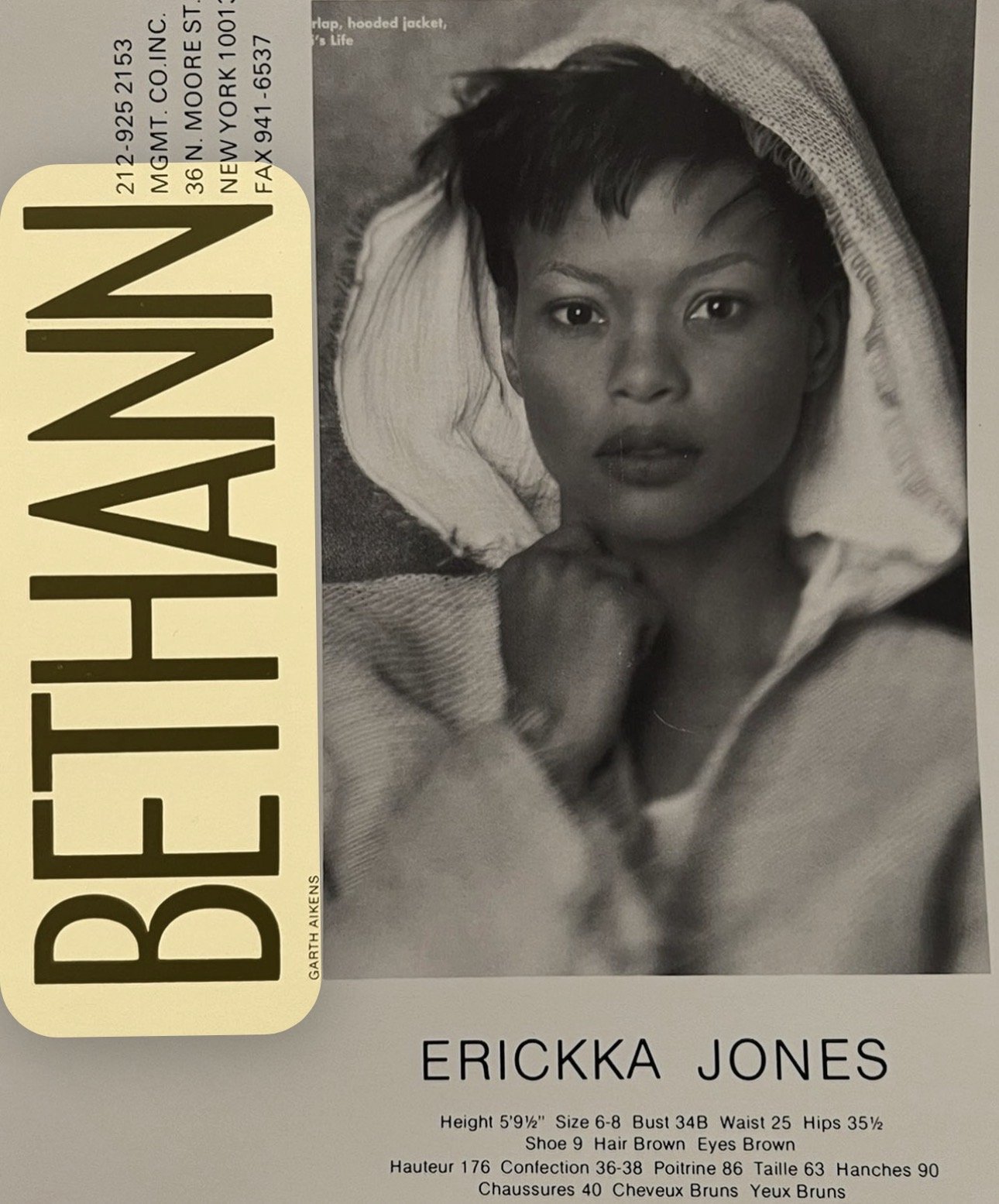 Black and white portrait photo of Erickka Jones, a young woman with short dark hair, looking directly at the camera with her hand resting on her chin, wearing a hoodie with a textured fabric on a Bethann modeling comp card. 