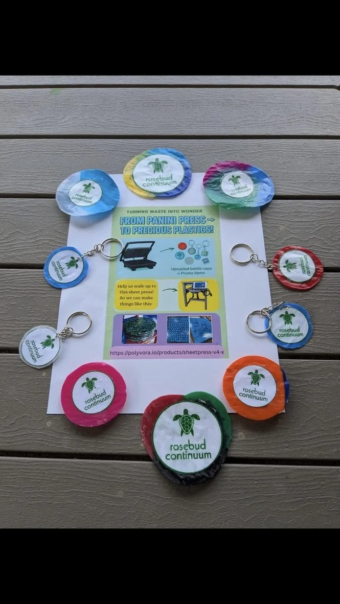 Colorful recycled bottle caps with 'rosebud continuum' logo, used as keychains, arranged around an informational sheet about turning waste into products.