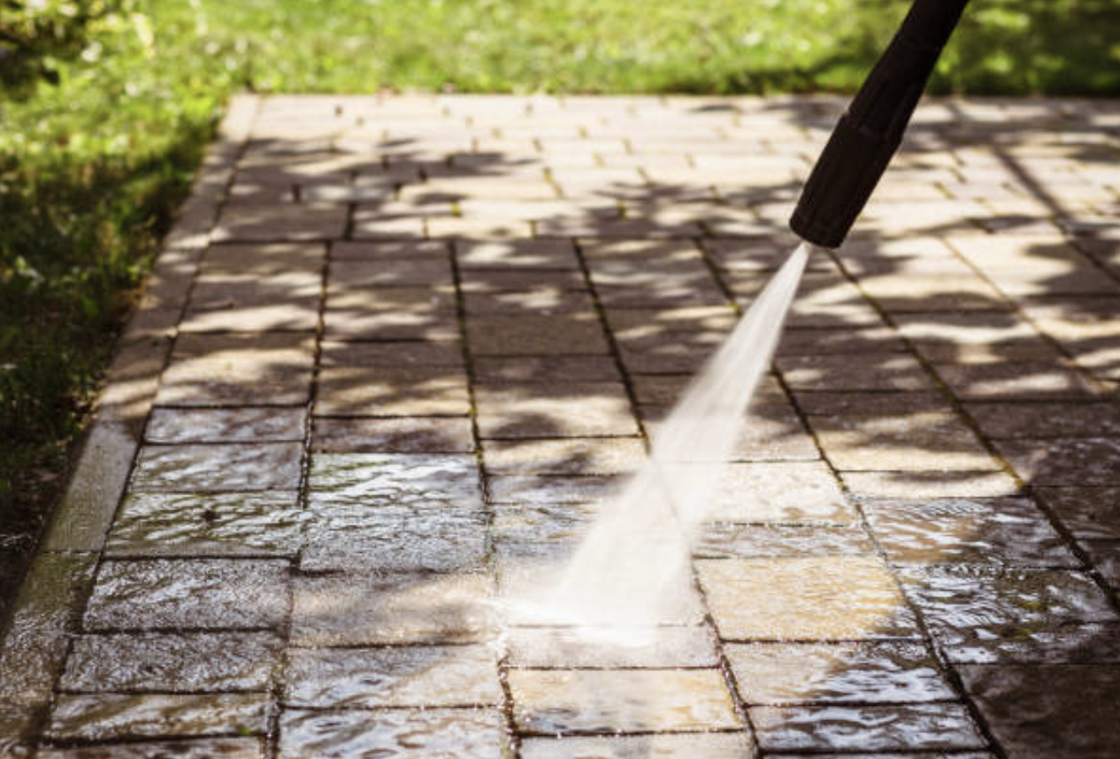A person Pressure washing a brick patio in daylight, with sunlight and shadows on the surface.