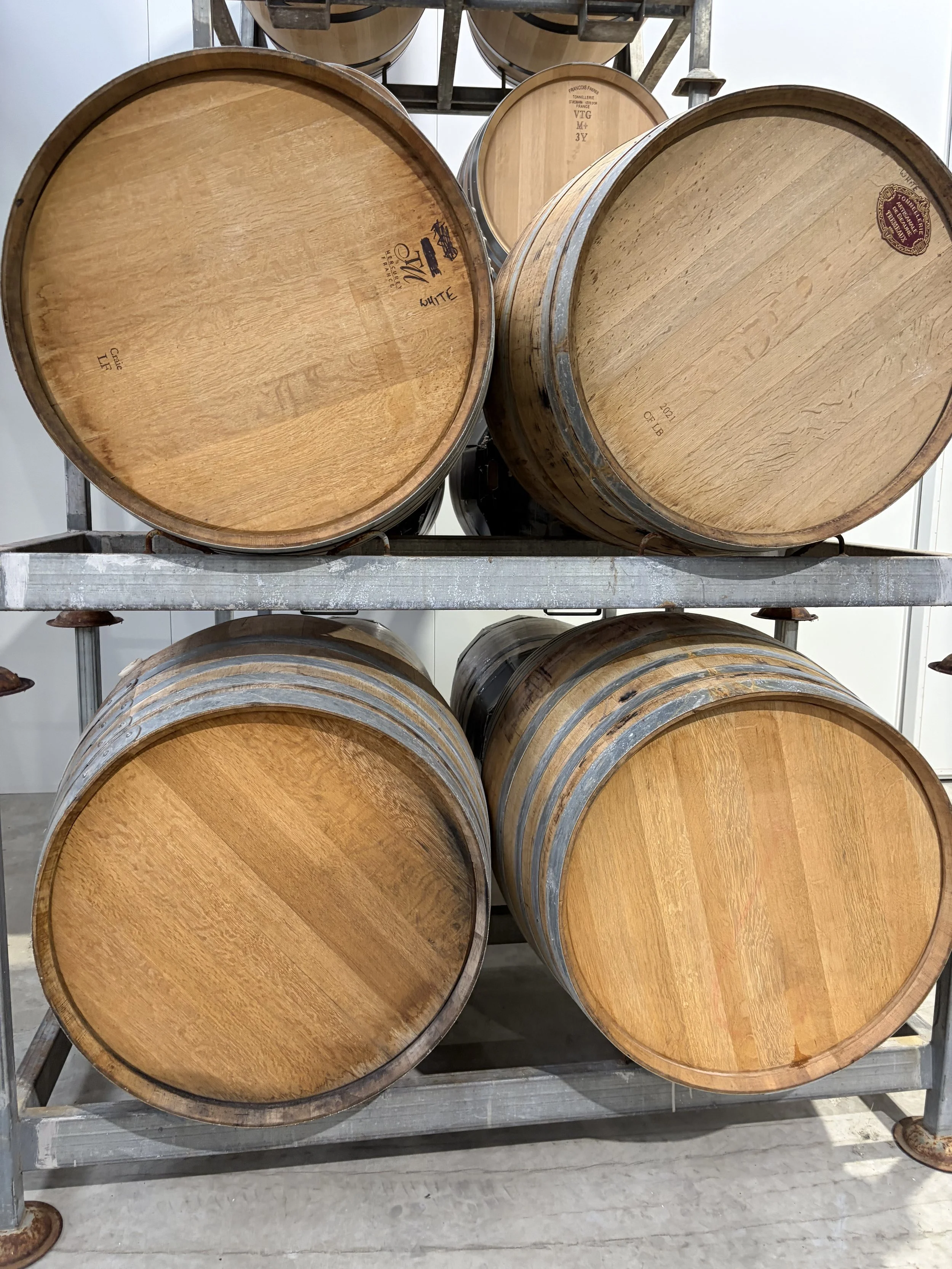 Wooden wine barrels on a metal rack in a winery or storage facility.