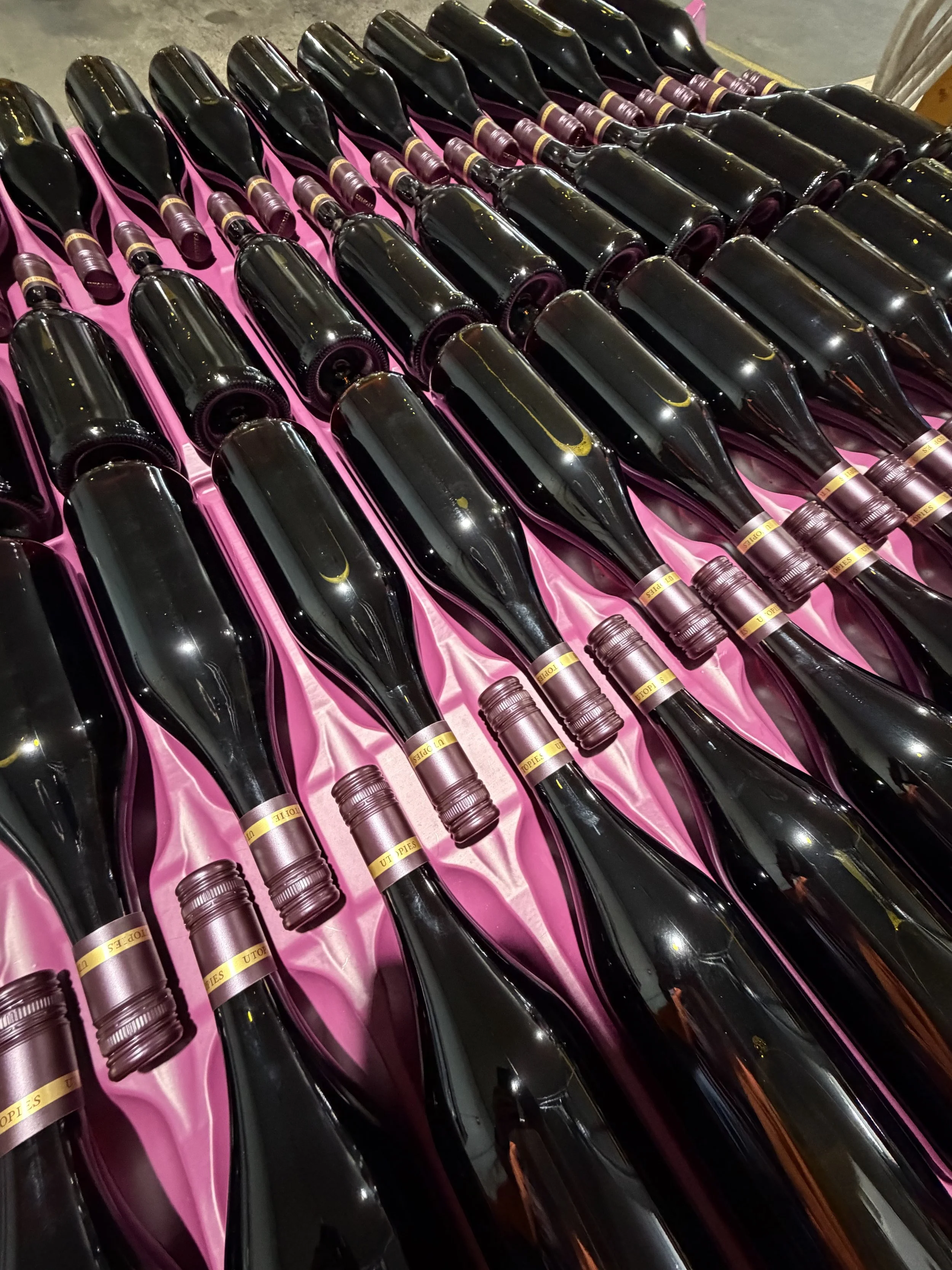 Multiple bottles of sparkling wine or champagne placed on pink satin fabric.