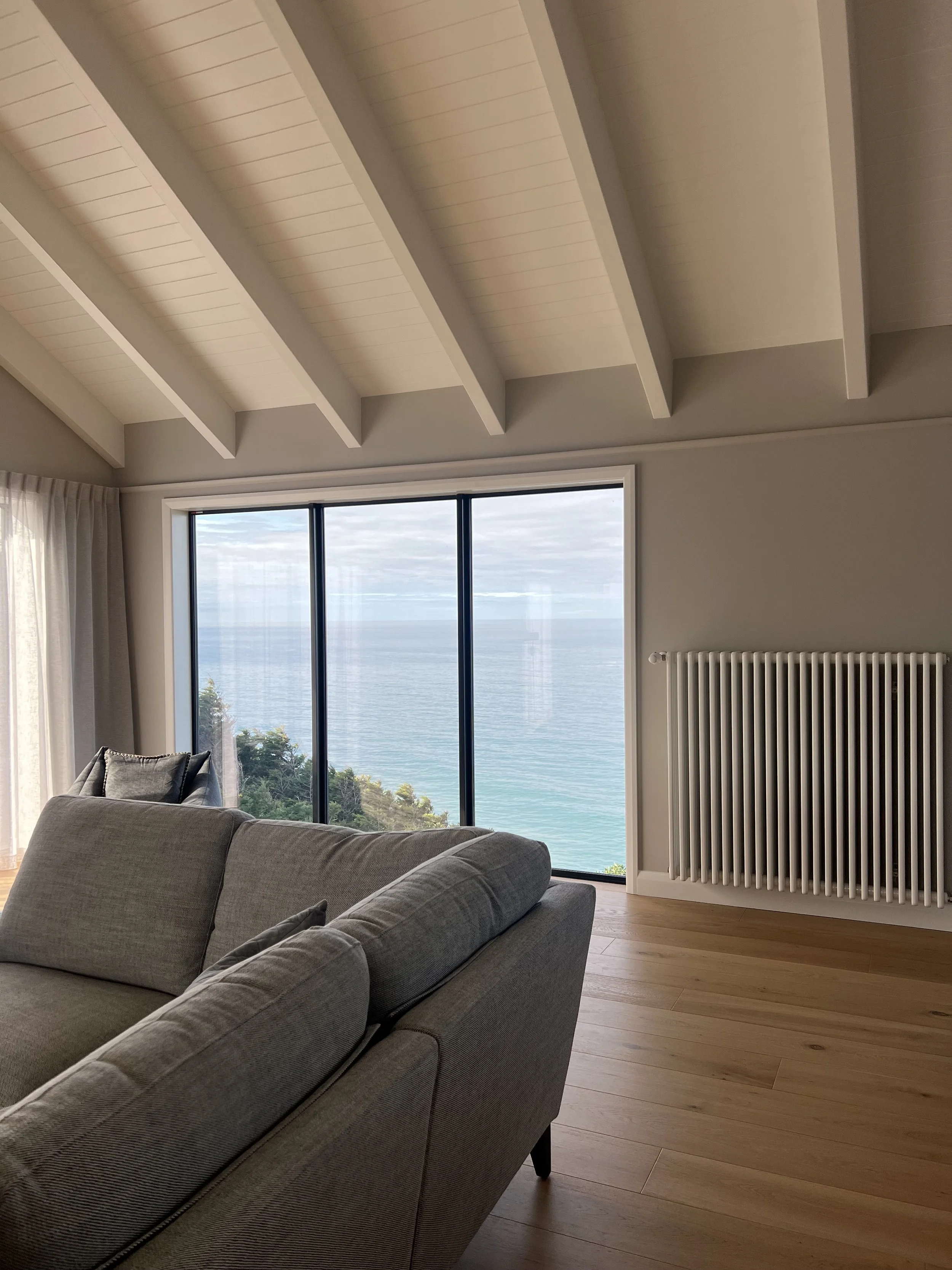 Picture of Living Room with Raked Ceiling, Wooden Floors, Linen Couch and View Out Window of the Ocean