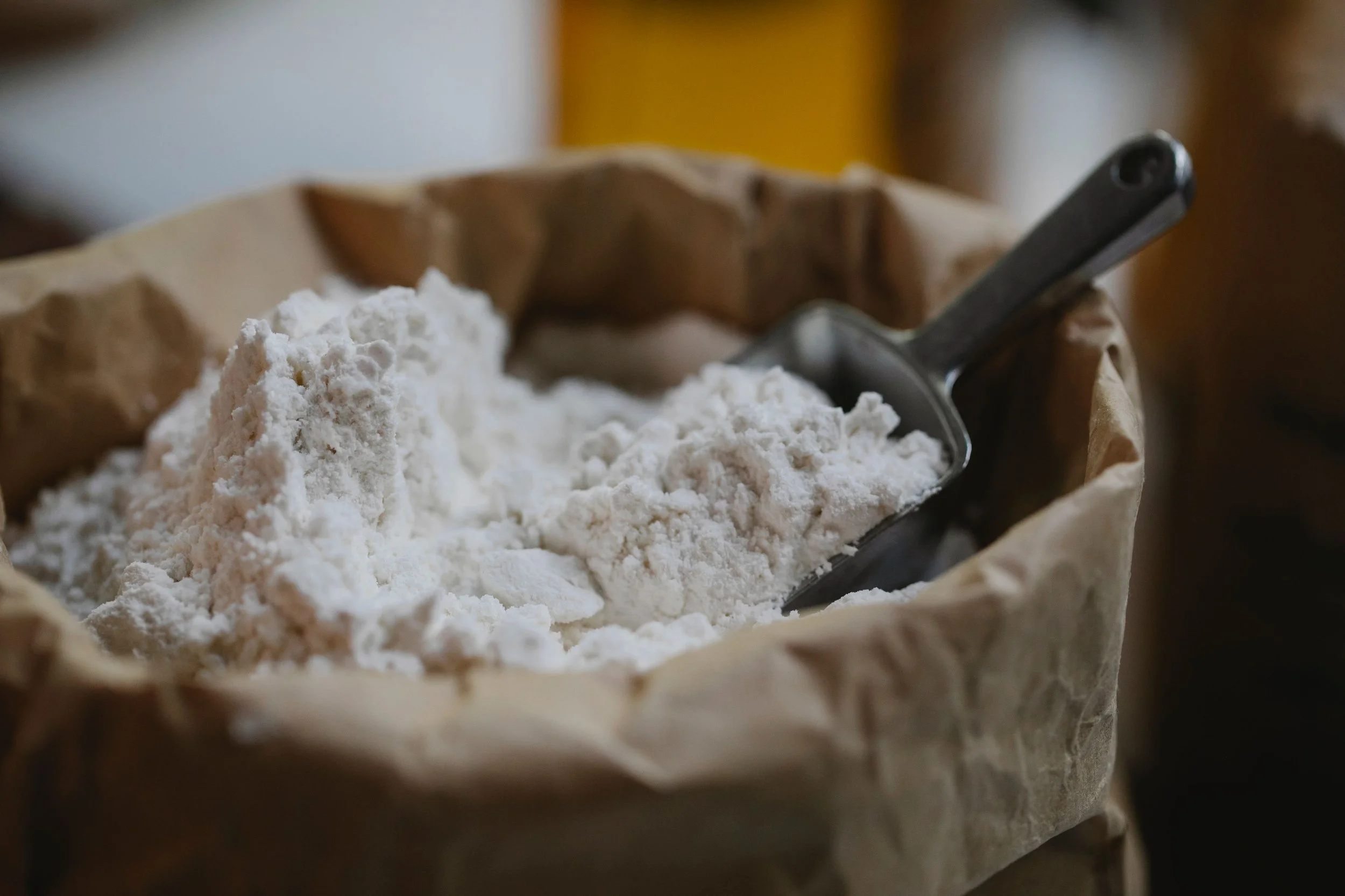 Organic, fresh-milled white flour in a brown paper bag with a metal scoop inside.