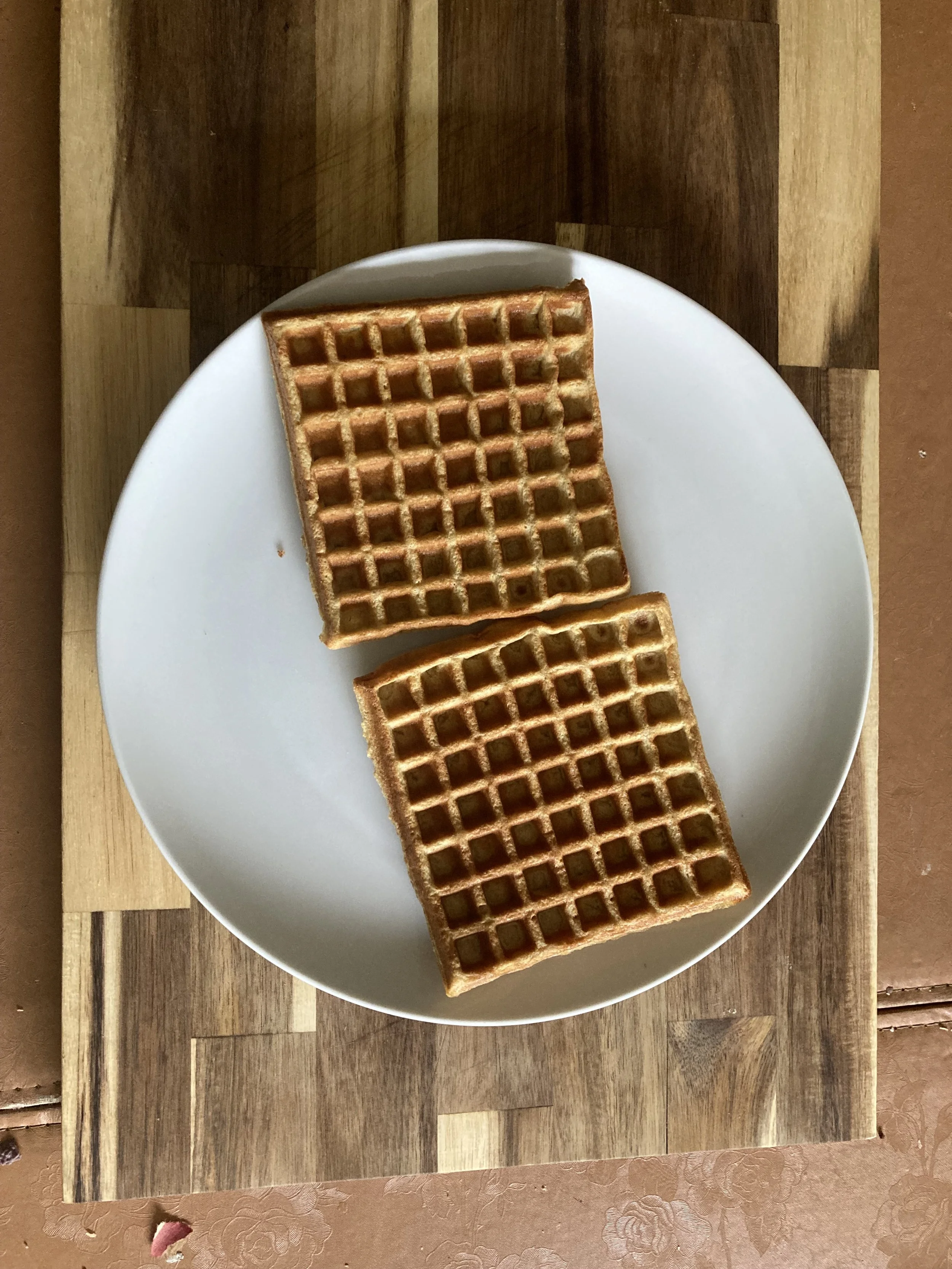 Two organic, fresh-milled einkorn waffles on a white plate sitting on a wooden table.