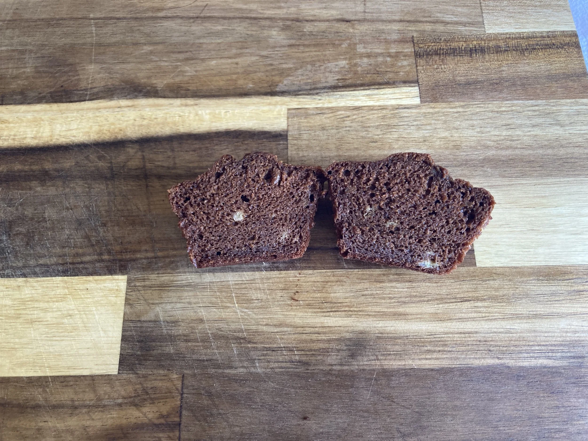 Two slices of organic fresh-milled Ezekiel flour chocolate banana muffins on a wooden cutting board