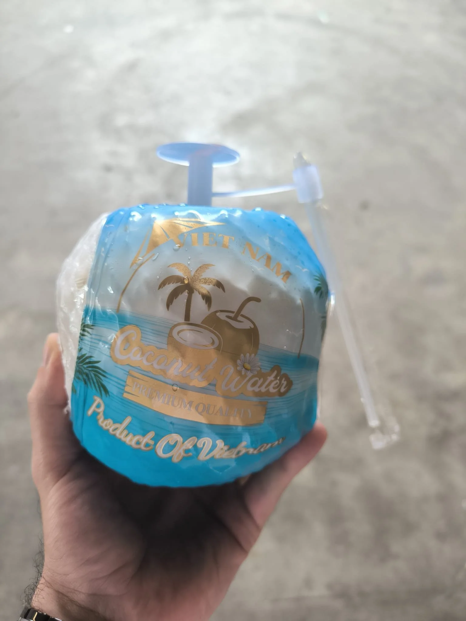 Hand holding an easy open drinking coconut with a straw against a factory floor background in Vietnam.