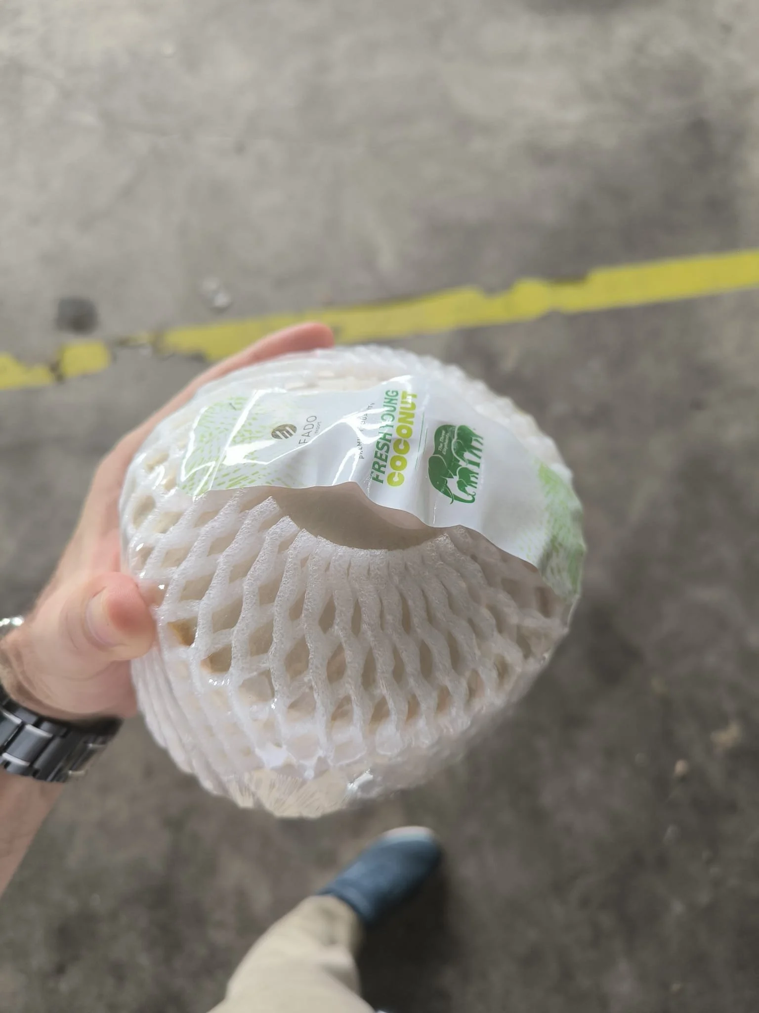 Person holding a bag of fresh young coconuts in an indoor parking lot with a yellow line on the concrete floor.