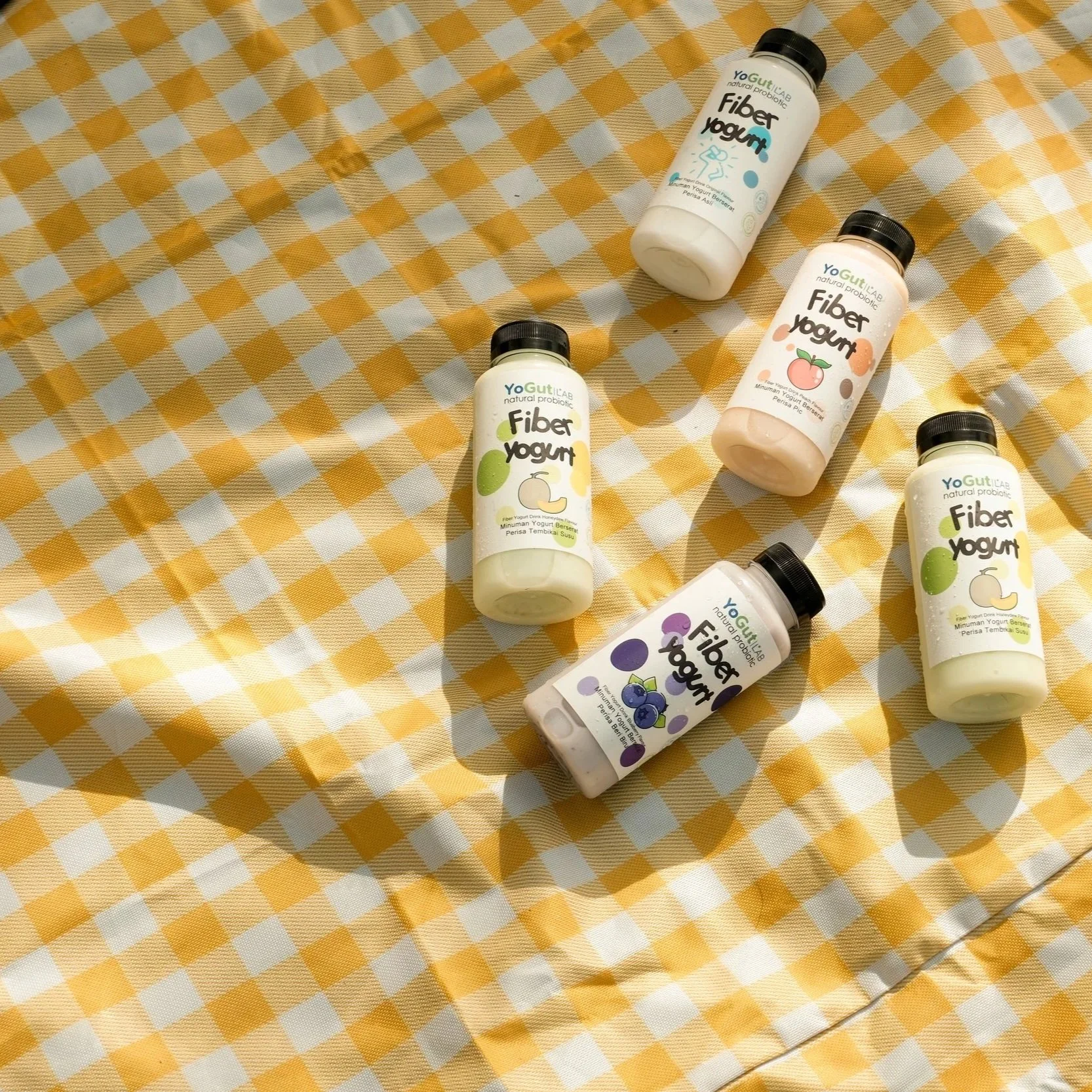 Multiple bottles of YogutLab's yogurt on a yellow and white checkered tablecloth.