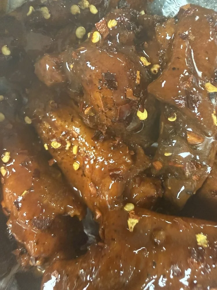 Close-up of cooked chicken drumsticks covered in a dark, glossy sauce with bits of chopped garlic and herbs visible.