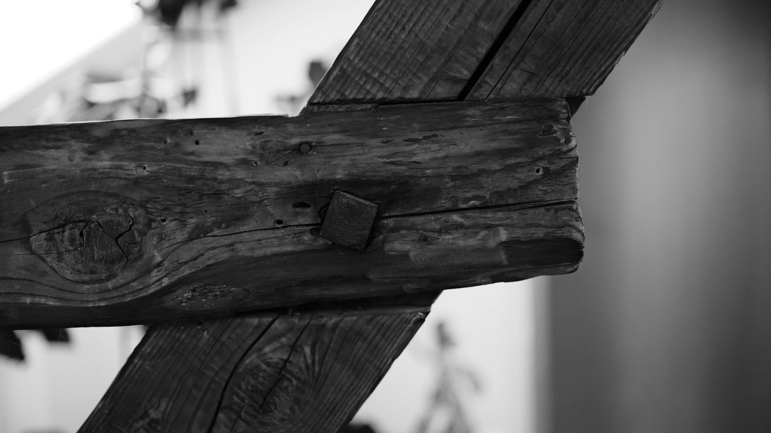 Nahaufnahme eines alten, wettergegerbten Holzbalkens, der mit einer Metallklammer befestigt ist, auf einem dunklen Hintergrund in Schwarz-Weiß.