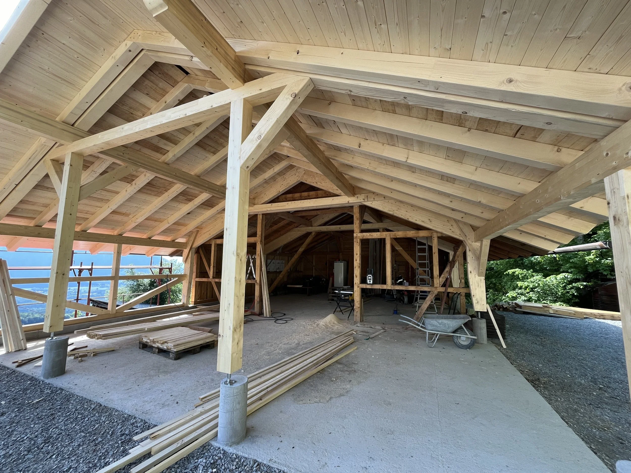 Holzrahmenbau eines Gebäudes im Bau, mit sichtbarem Dachstuhl aus Holz und Baugerüsten im Hintergrund.