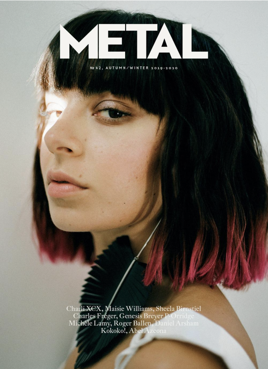 Magazine cover of METAL with a close-up of a young woman with black hair with pink tips, wearing a black pleated accessory, and a white top.