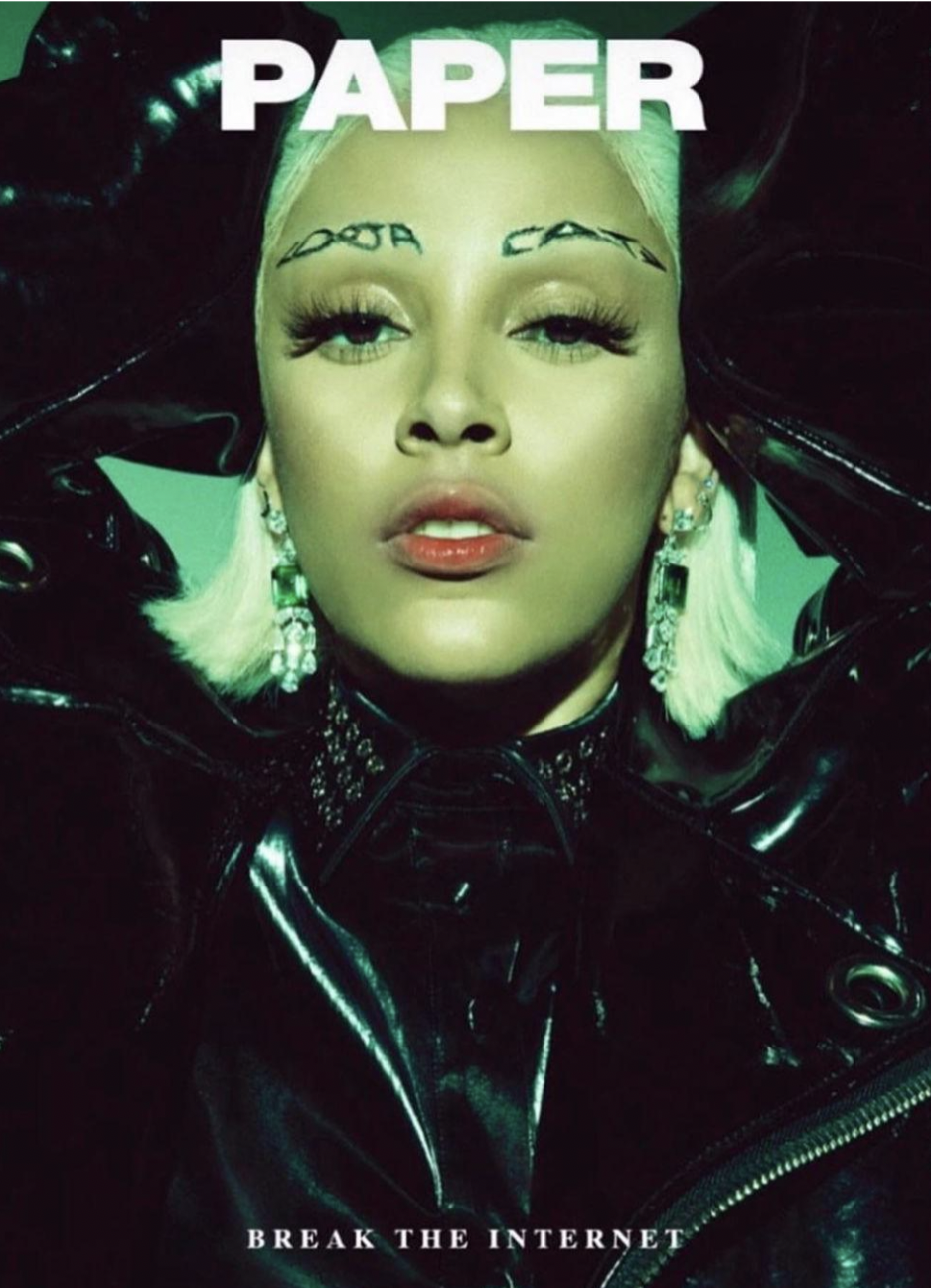 A woman with platinum blonde hair and tattoos above her eyebrows that say 'DOPE' and 'CATA,' wearing large earrings, bold makeup, and a black shiny jacket. The word 'PAPER' is at the top, and 'BREAK THE INTERNET' is at the bottom.