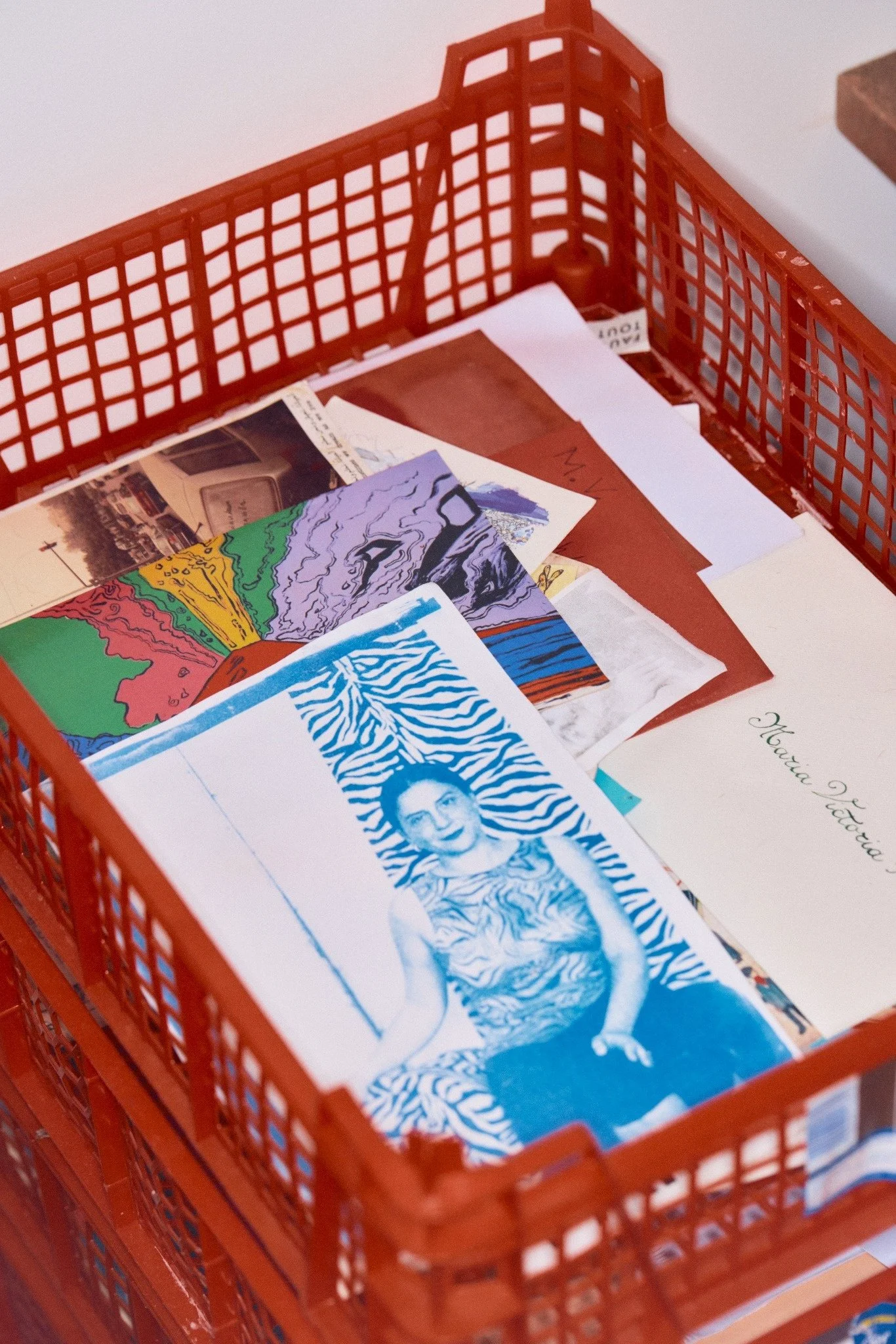A red plastic shopping basket filled with various colorful booklets and papers, with a partially visible wooden surface in the background.