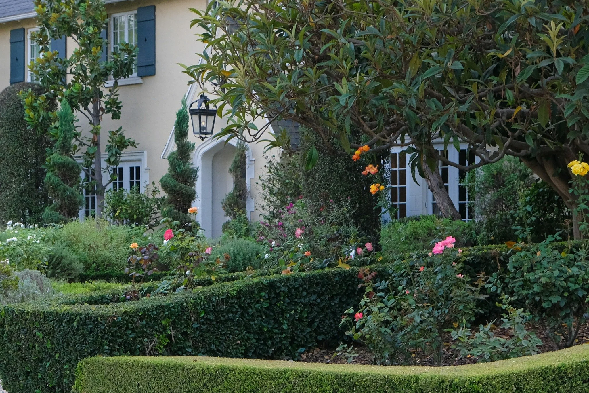Manicured garden and flowering hedges surrounding a secluded country house with shuttered windows and a private entrance.