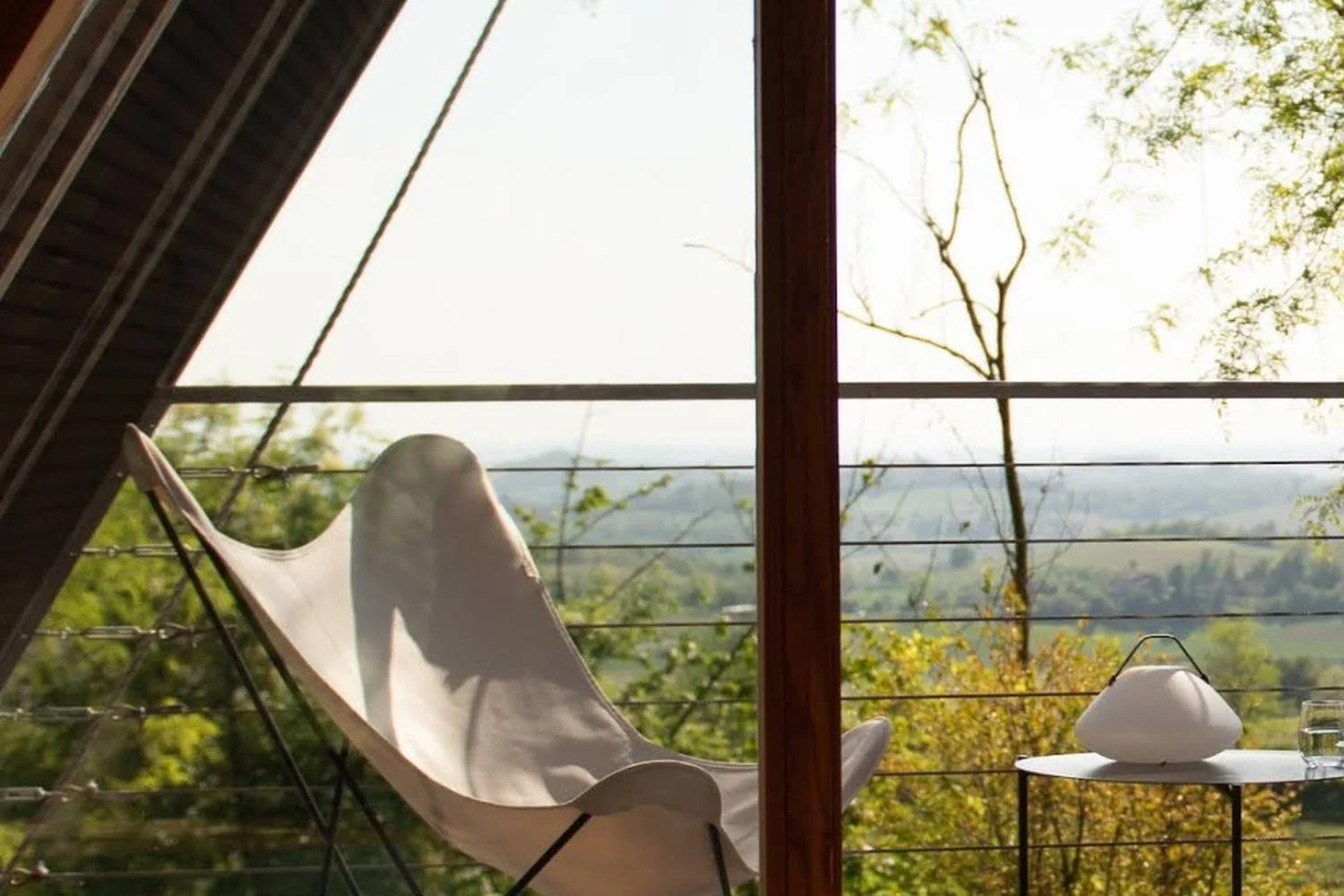 Empty lounge chair and side table on a sunlit retreat terrace overlooking a peaceful green landscape.