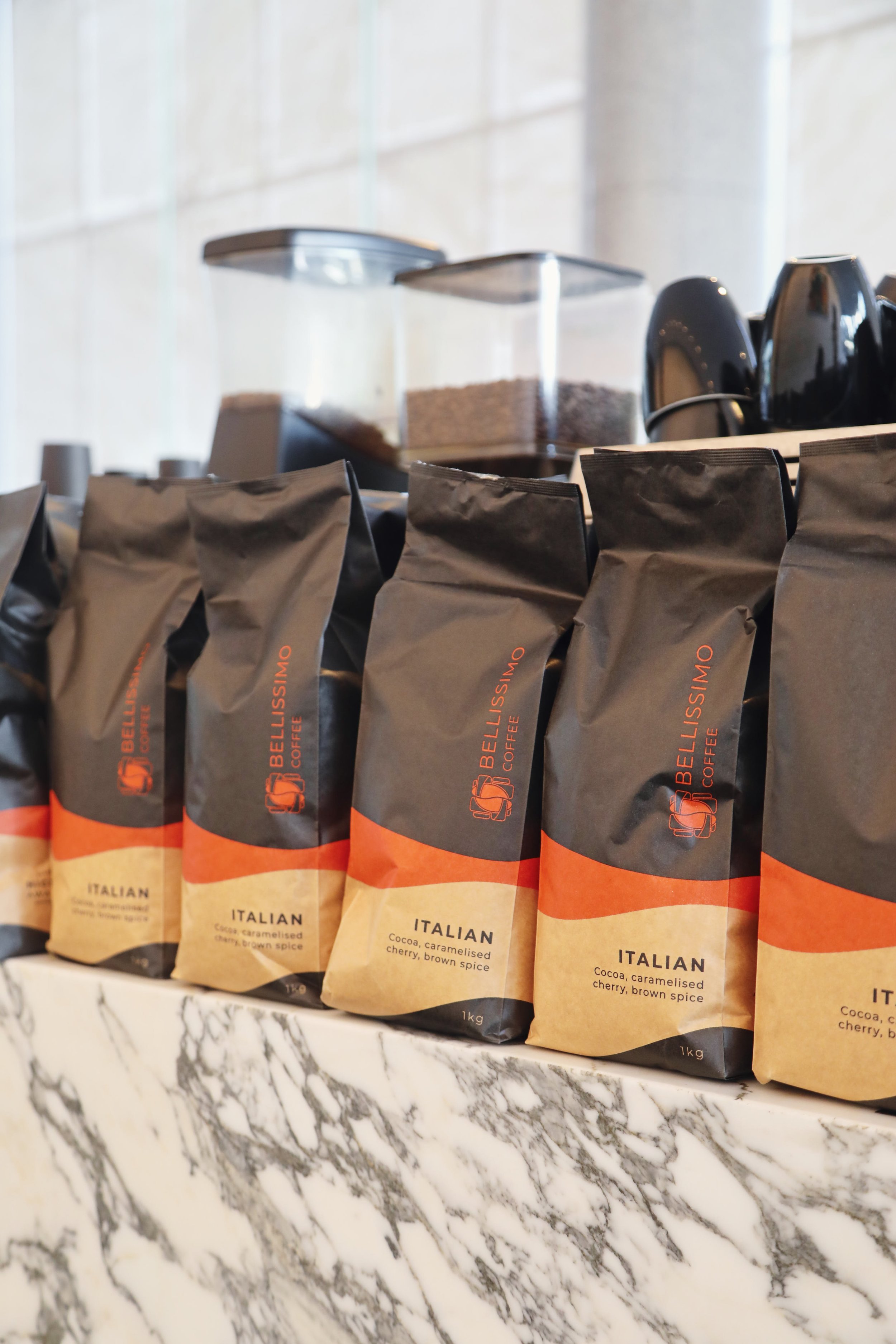 Arrangement of Italian flavored coffee or cocoa products in black and orange packaging on a marble surface with dispensers in the background.