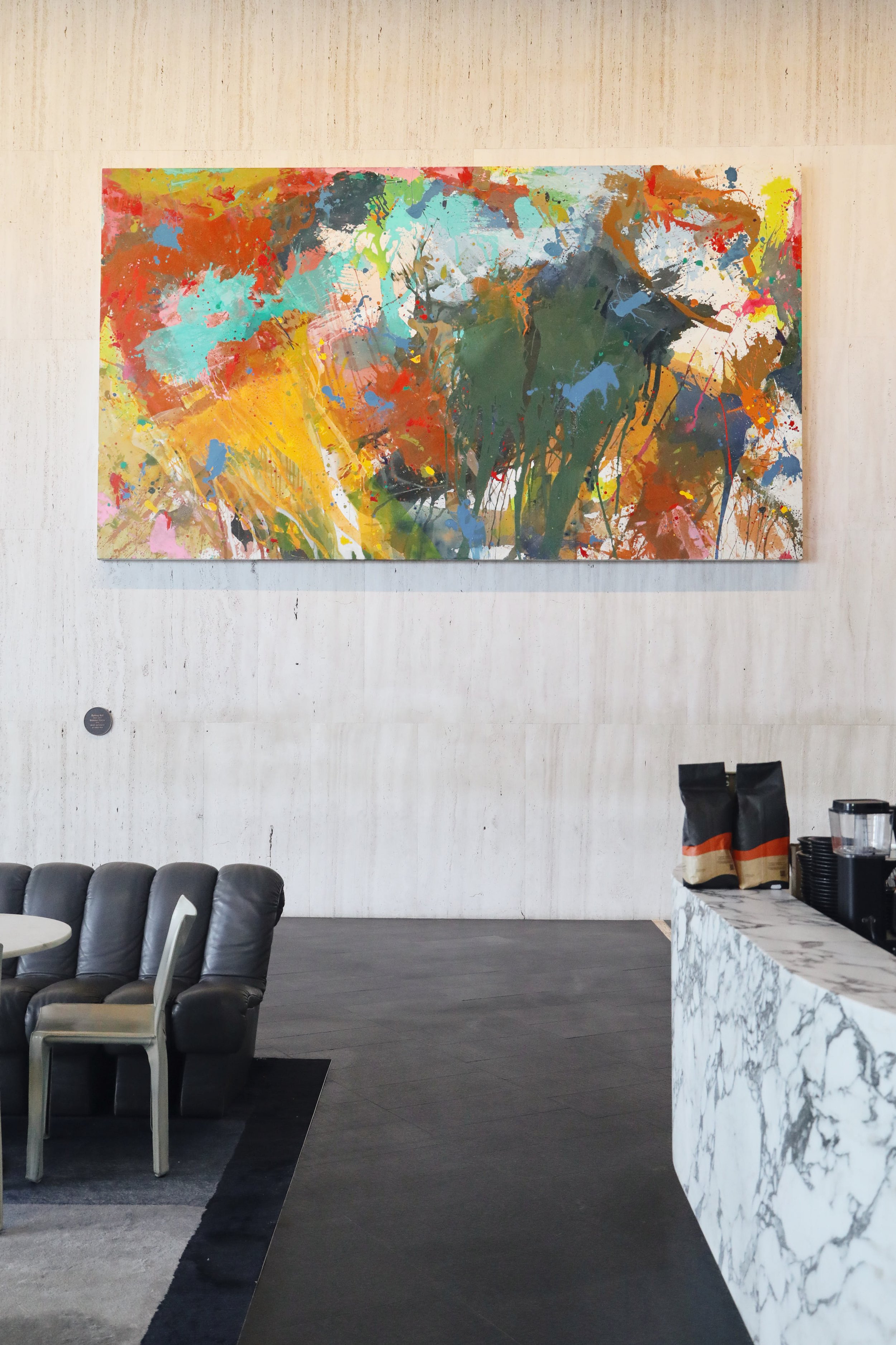 Abstract colorful painting hanging on a beige wall in a modern cafe with a marble counter and black chairs.