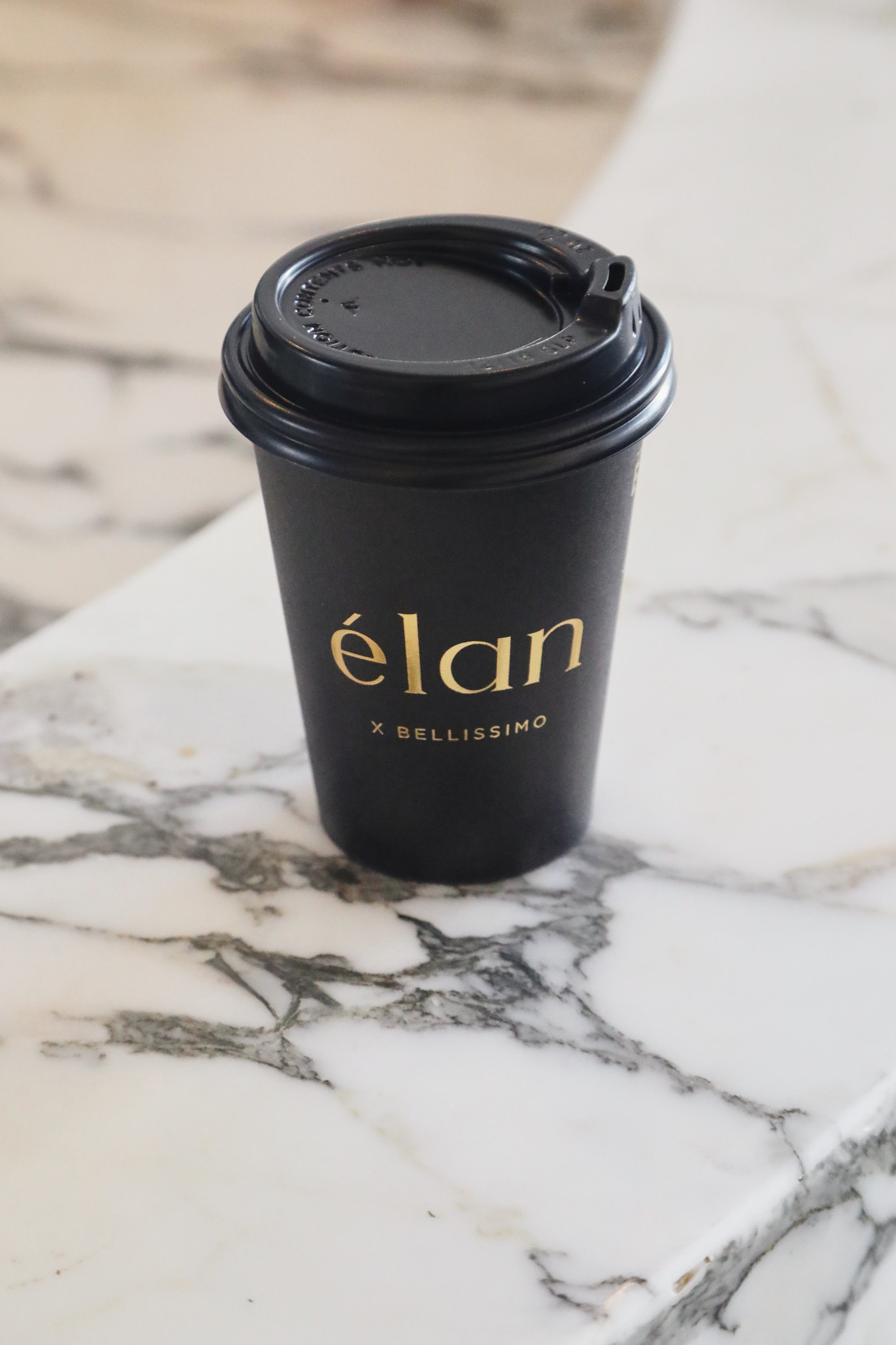A black disposable coffee cup with a plastic lid on a white marble surface.