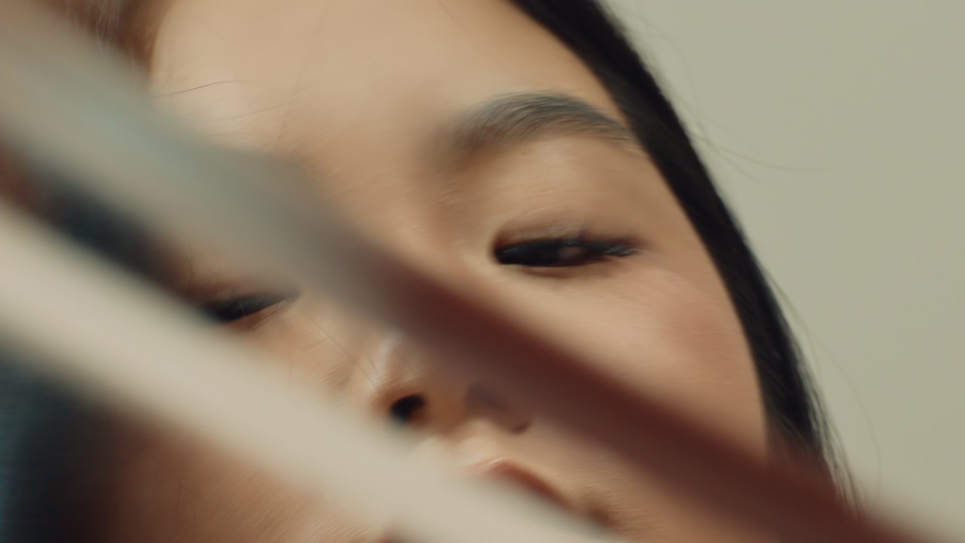 Close-up of a person's face with eyes closed, partially obscured by a blurred object in the foreground.