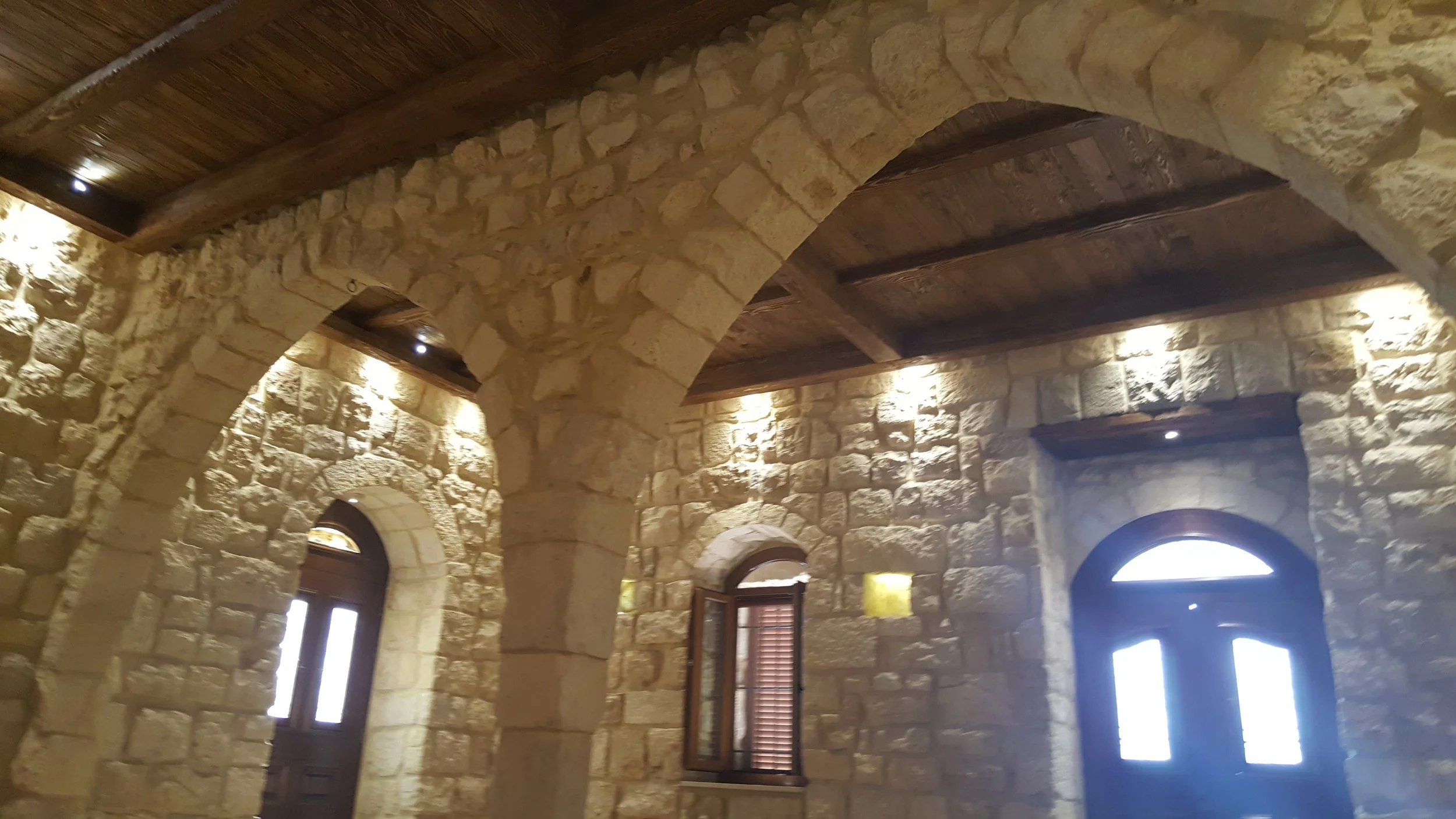 Interior of a stone building with arches, high wooden ceilings, and small windows.