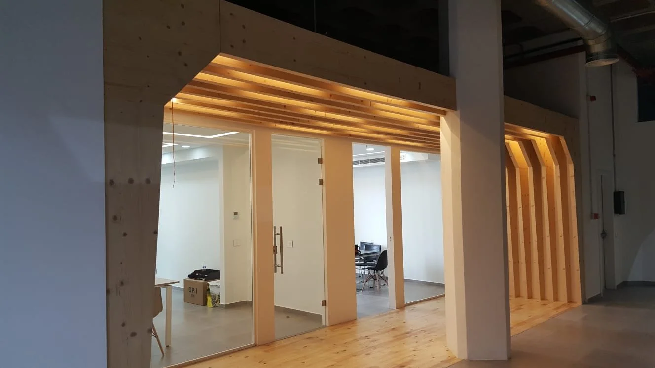 Modern office space with glass walls, wooden framing, and minimalist furniture.