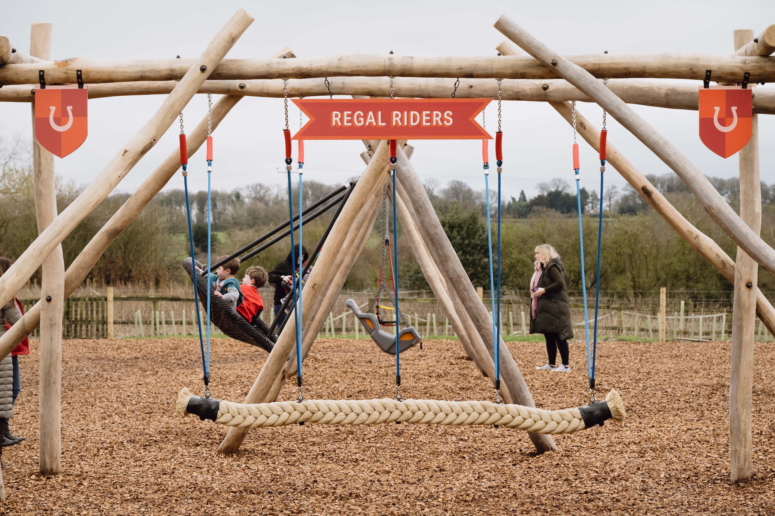 The Regal Riders outdoor rope swing play area featuring vibrant red custom illustrated signage with bold typography.