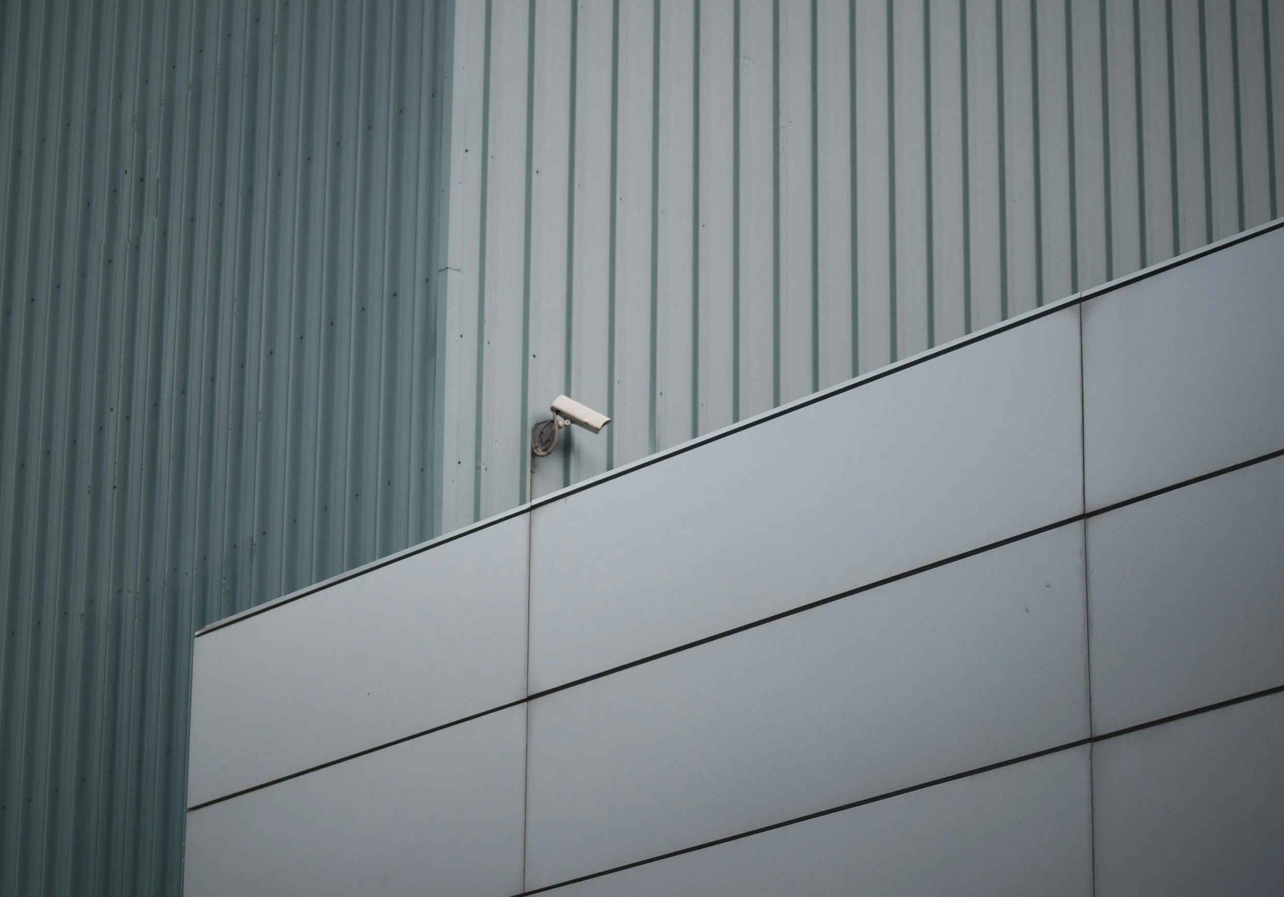 Close-up shot of a modern security camera mounted on a corrugated metal wall, with architectural elements.