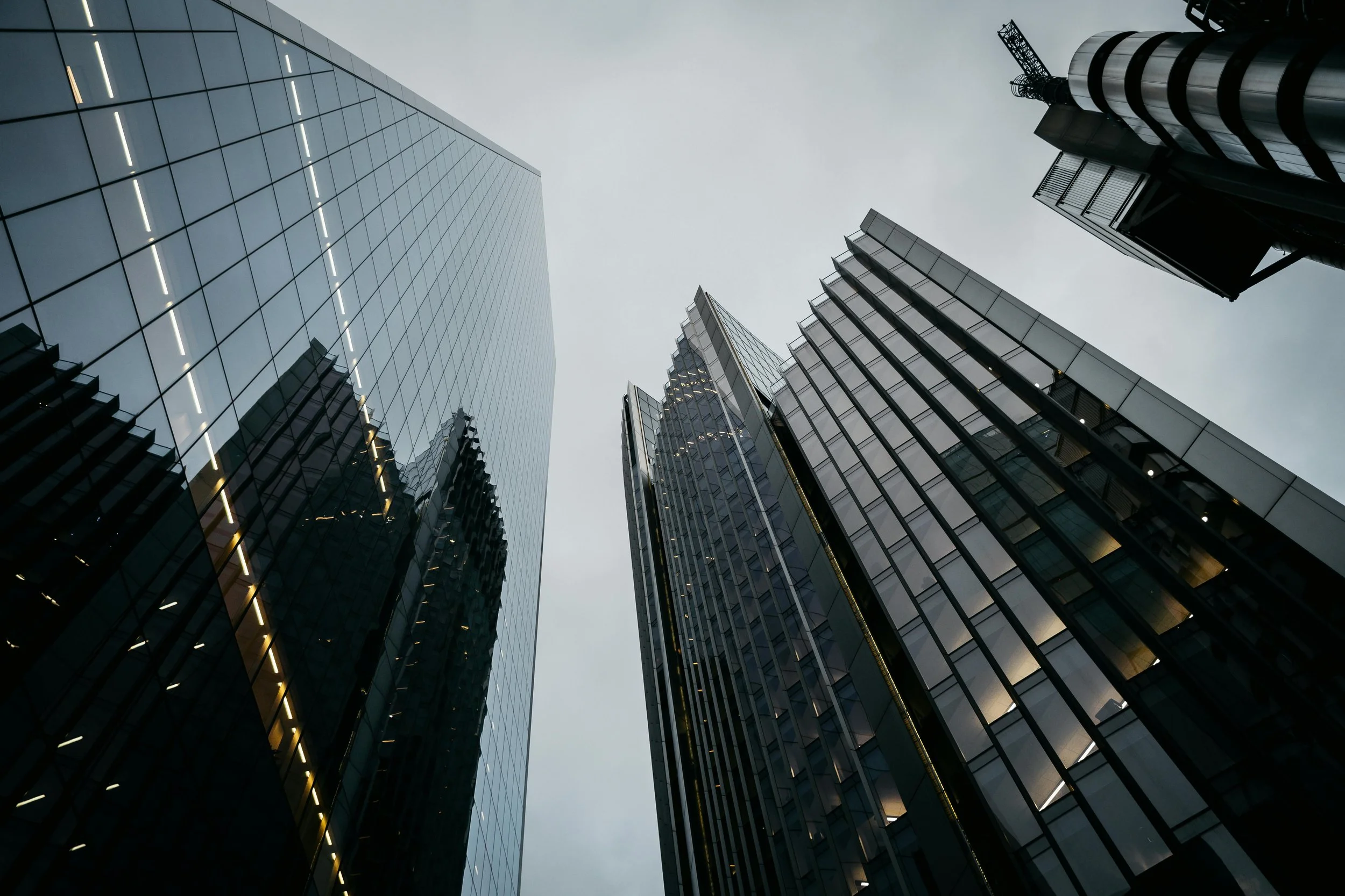 Low-angle architectural view of sleek city skyscrapers stretching up into a dramatic, overcast sky.