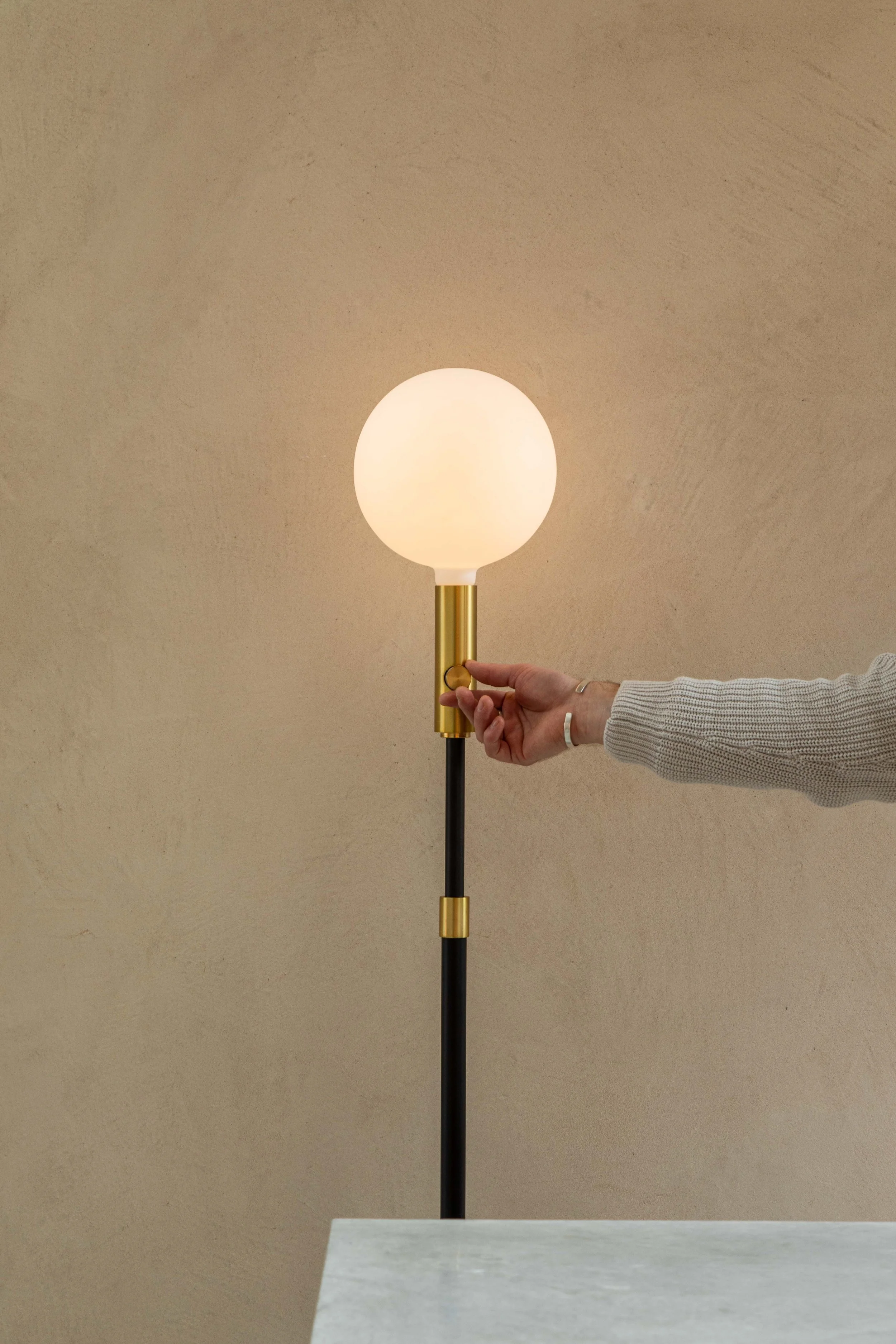 Tala adjustable floor lamp emitting a soft glow, set against a minimalist taupe wall.