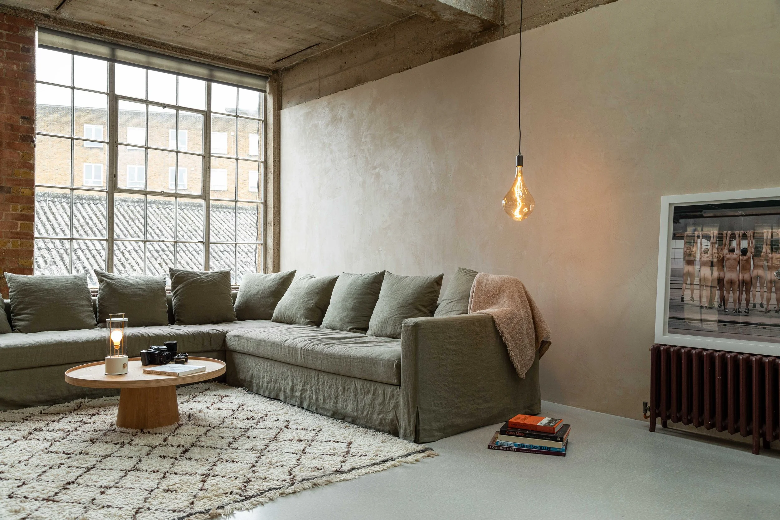 Minimalist living room with an olive green sofa and an elegant Tala pendant light fixture.