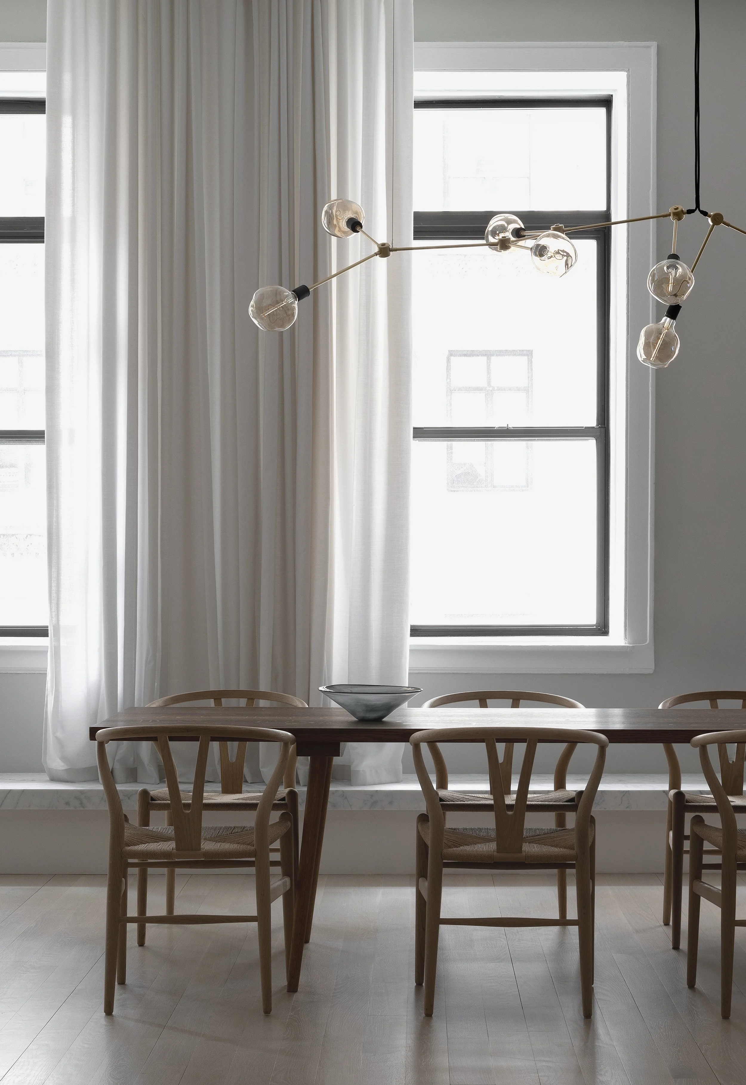 Minimalist dining room with airy curtains where an elegant Tala ceiling chandelier hangs over the table.