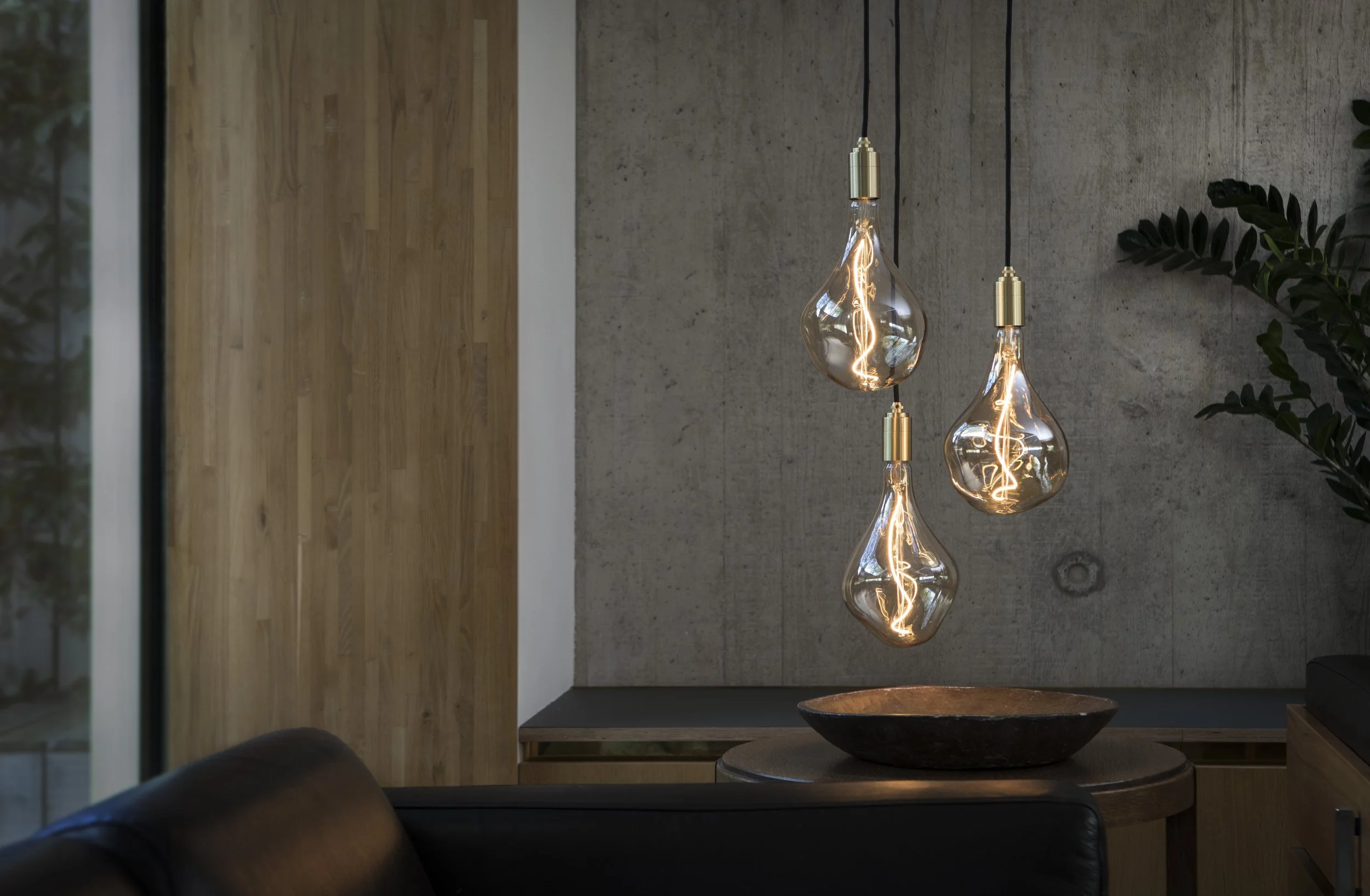 Three Tala pendant lights hanging above a small dining table with a fruit bowl, against an exposed concrete wall.
