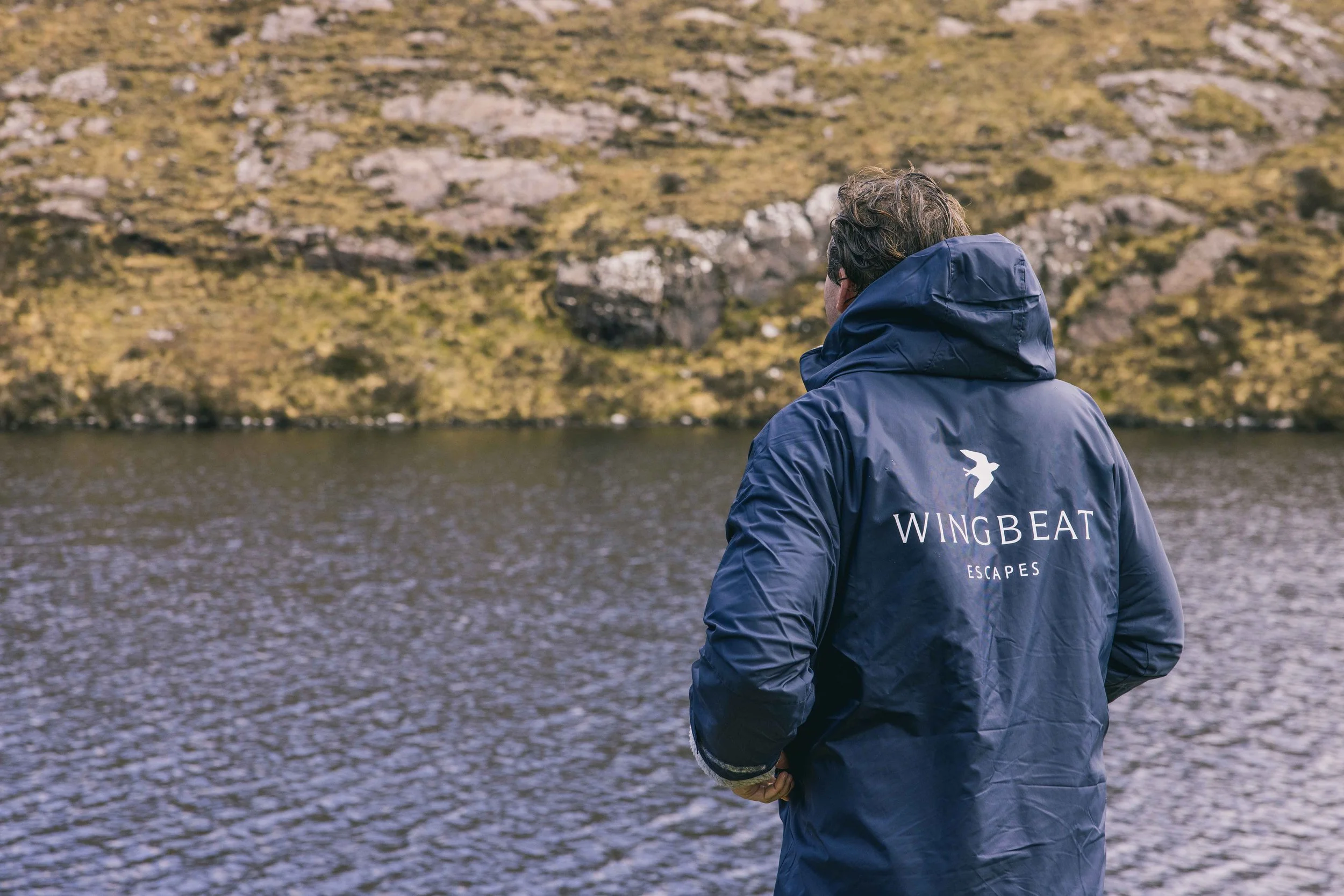 A customer wearing a Wingbeat Escapes branded raincoat, standing by a scenic Scottish loch.