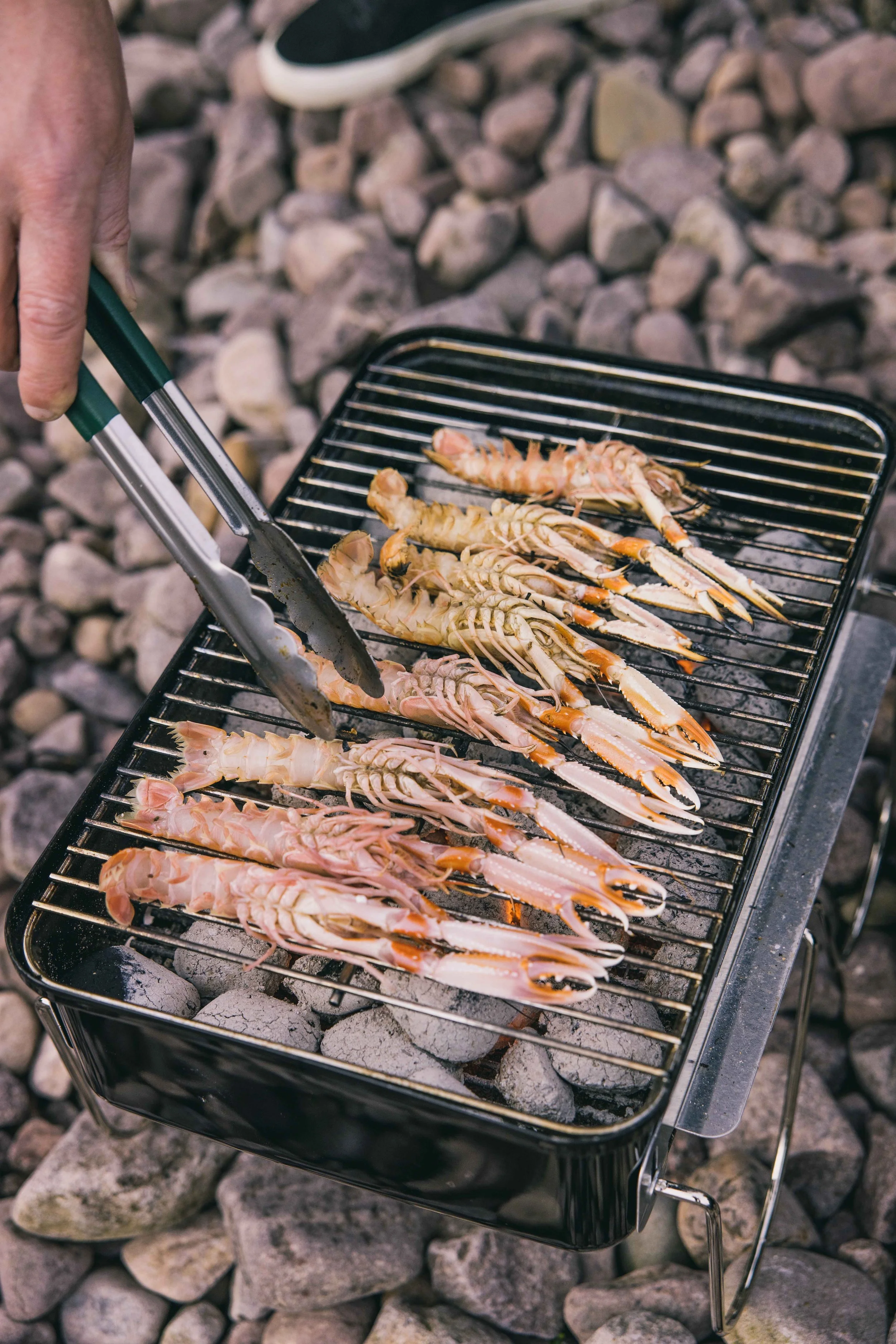 Close-up of a Wingbeat Escapes customer cooking fresh langoustines on a charcoal grill.